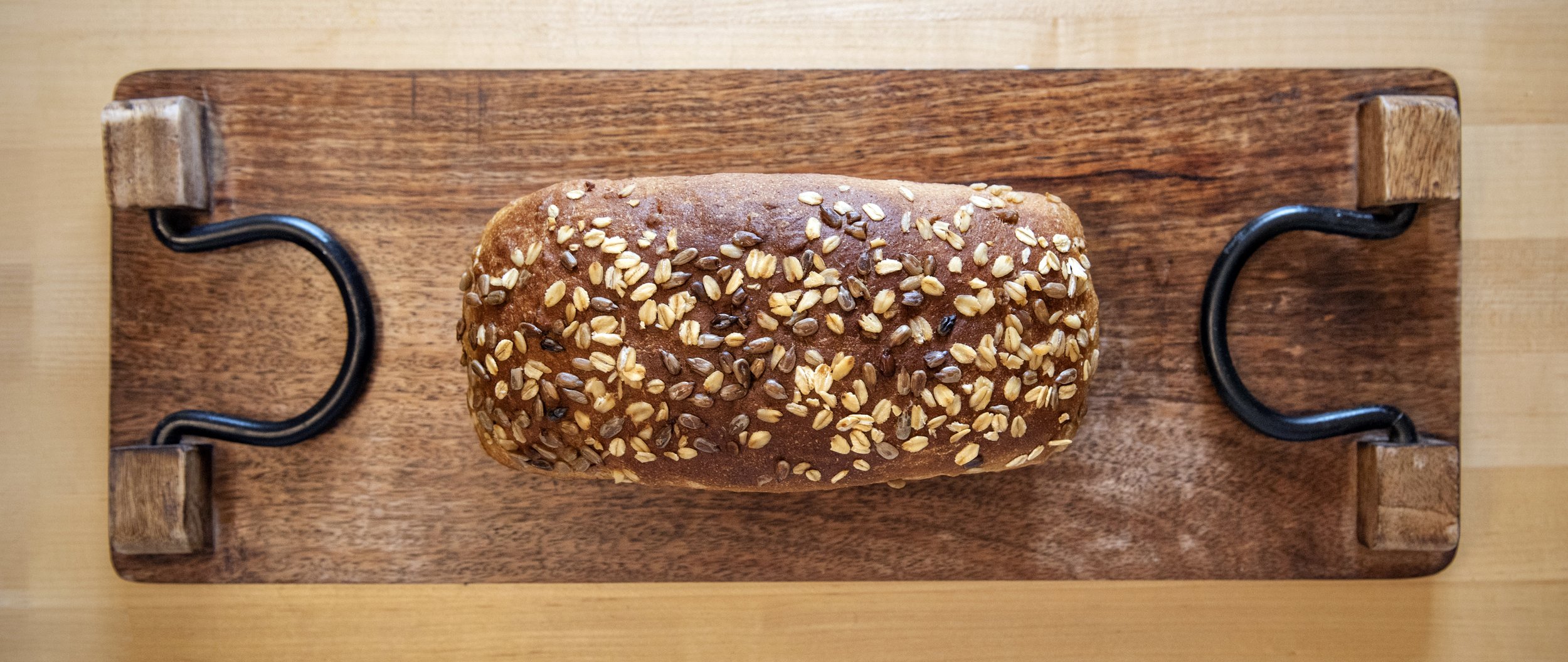Top view of a loaf of bread topped with mixed seeds placed on a wooden serving board.