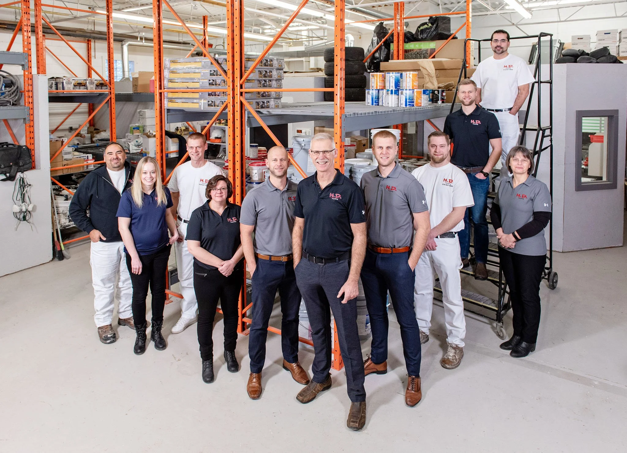 Group of workers standing inside a warehouse with orange shelves filled with supplies and equipment.