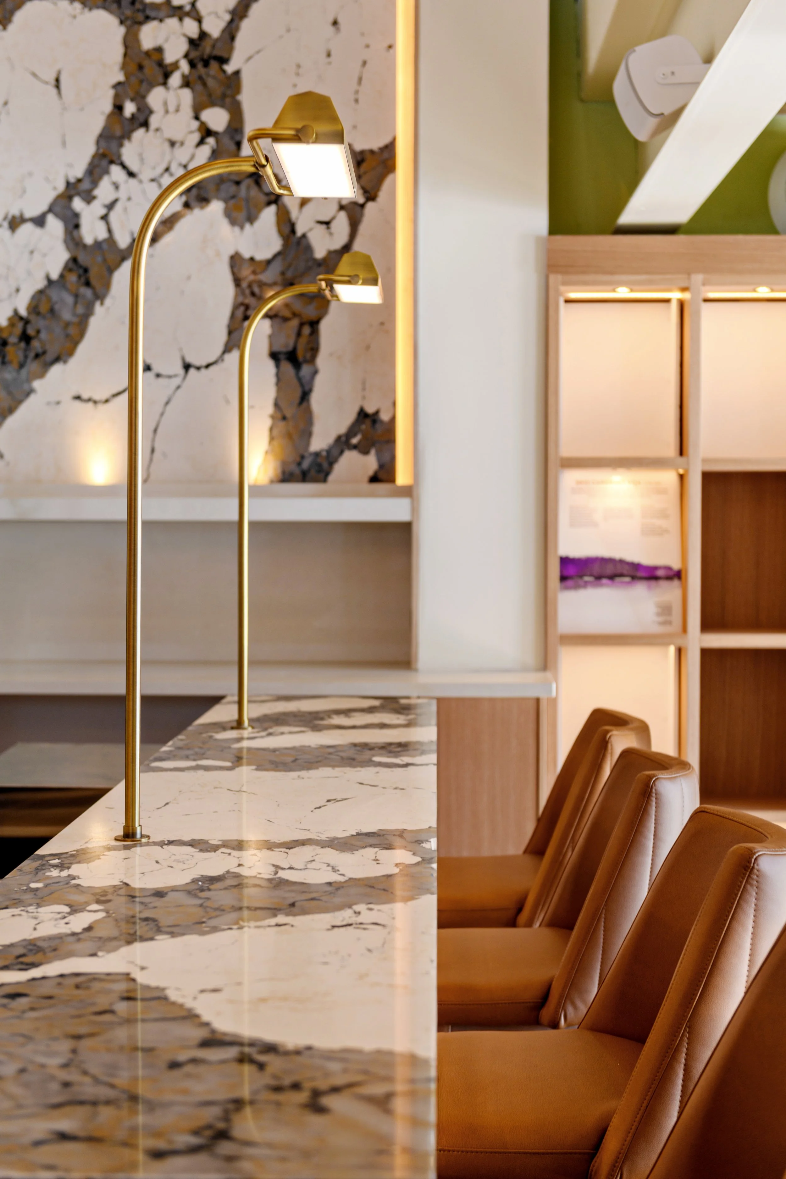 A modern interior space with a marble countertop, gold reading lamps, and brown leather chairs.