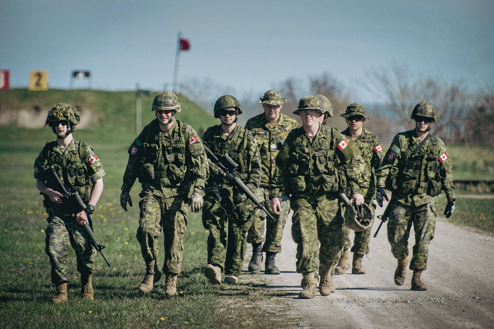 A group of soldiers in camouflage uniforms and helmets walking in formation outdoors on a sunny day.