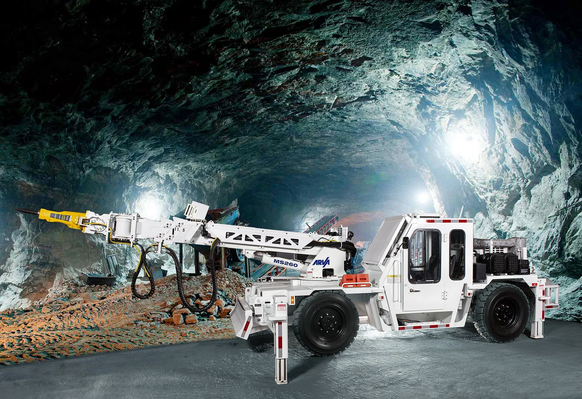 Underground mining tunnel with mining equipment, including a large white drilling vehicle and a small vehicle, illuminated by artificial lights.