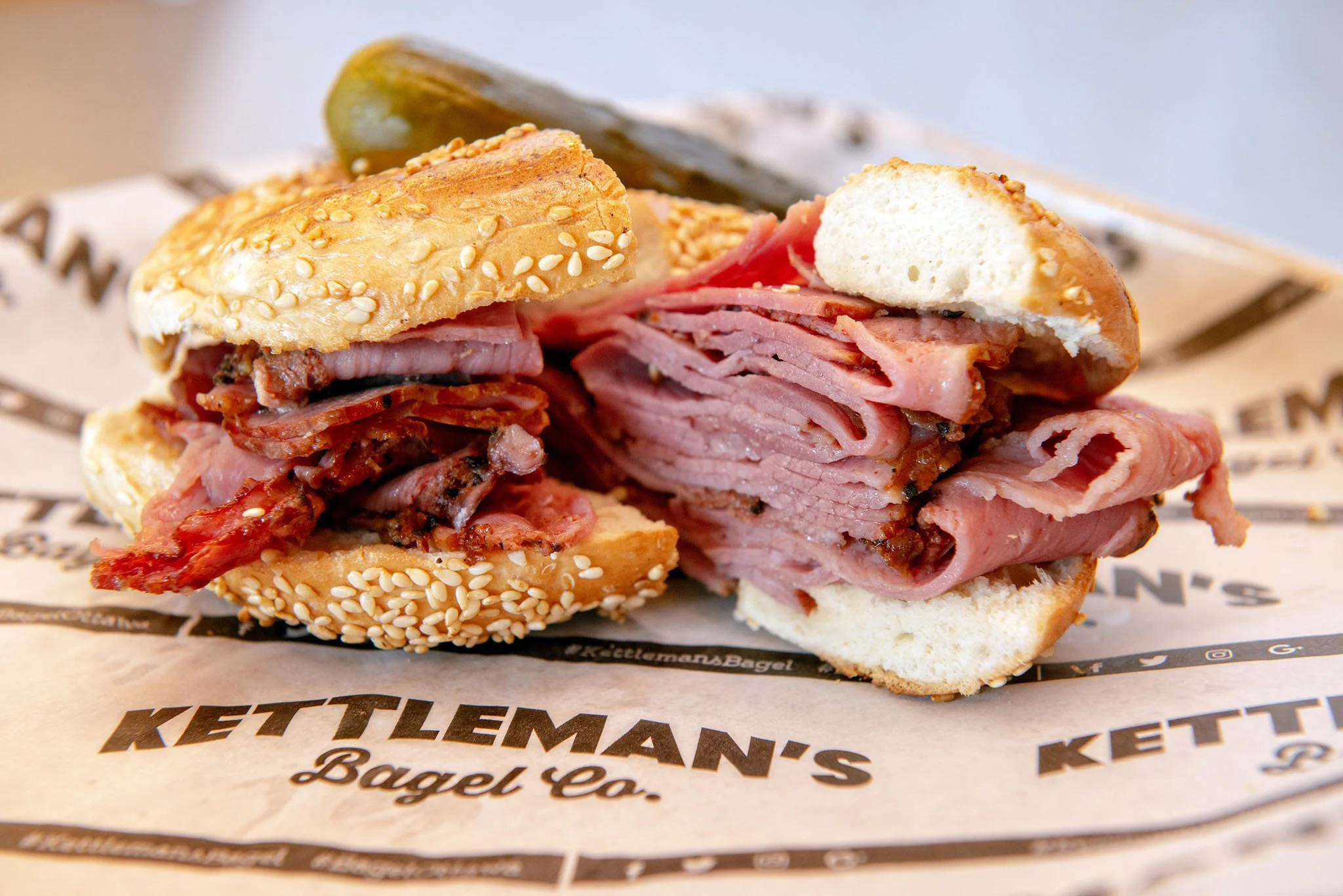 Close-up of a sandwich with sliced ham, bacon, and sesame seed bun on branded paper