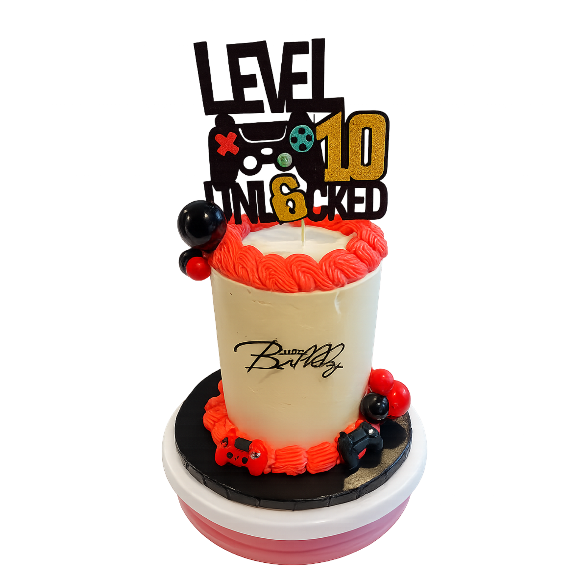 Birthday cake with red and black decorative icing, topped with a cake topper reading 'Level 10 Unlocked' and featuring gaming controller accents and colorful balls.
