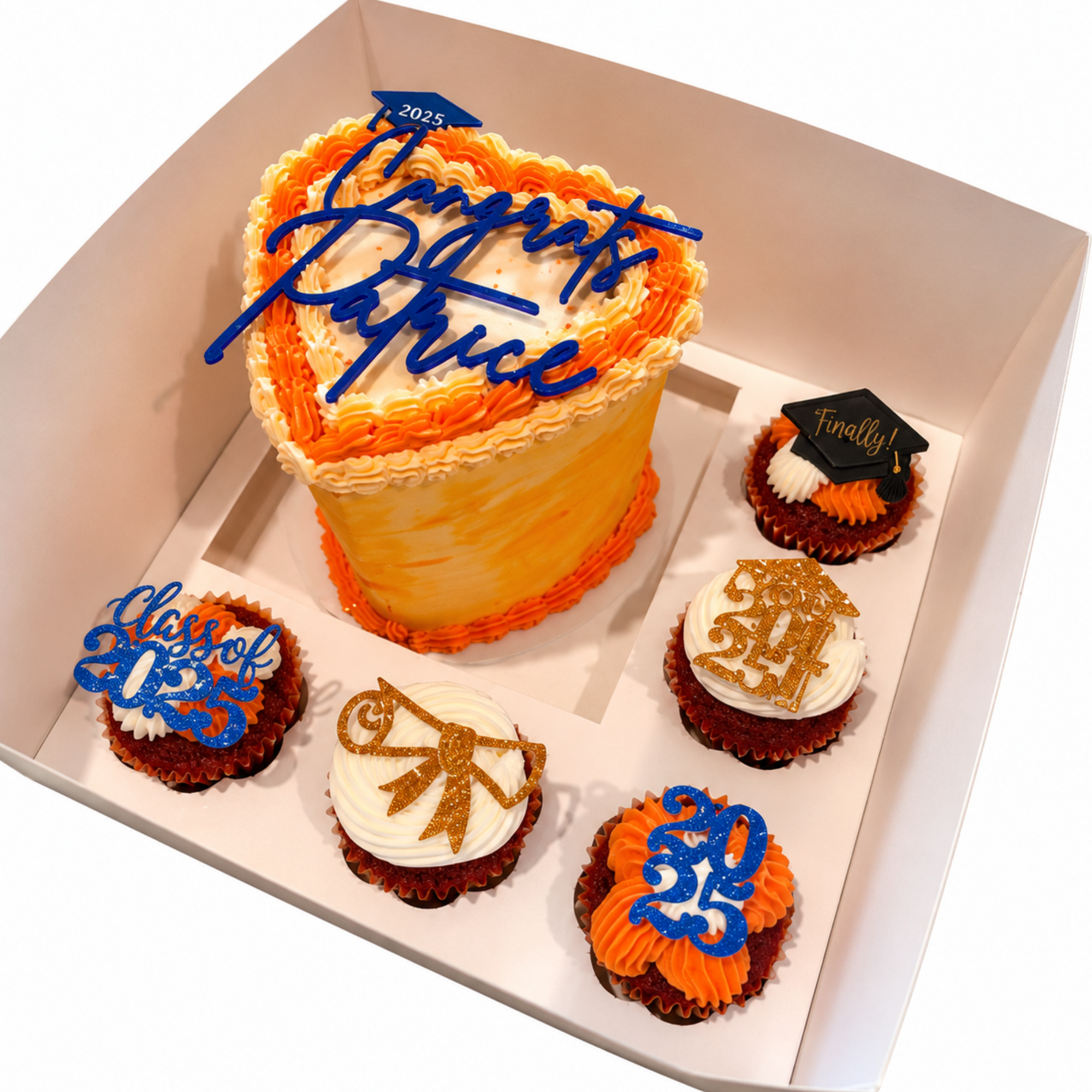 A decorated cake celebrating graduation with orange and white frosting and a blue 'Congratulations Grad' topper, surrounded by cupcakes with graduation-themed decorations.