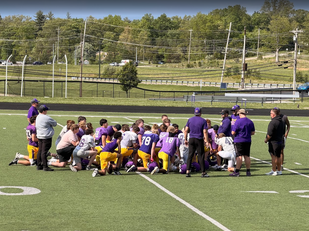 Football team gathered on the field during a practice or game, with coaches giving instructions.