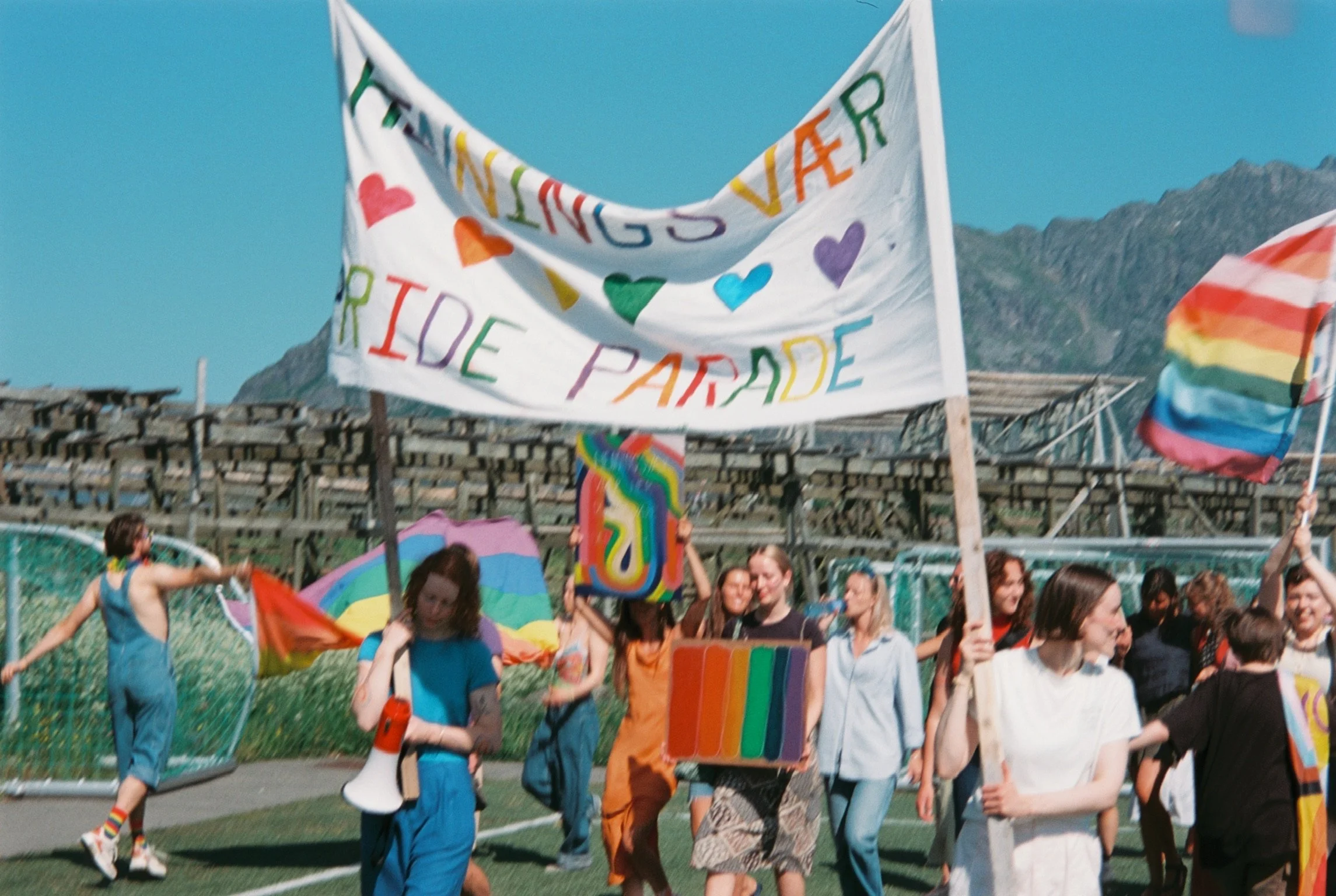 Folk som deltar i en parade med regnbuefargede flagger og en banner som sier 'Love is Love'.