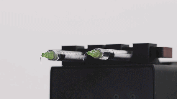 Two syringes filled with liquid, resting on a black surface against a white background.