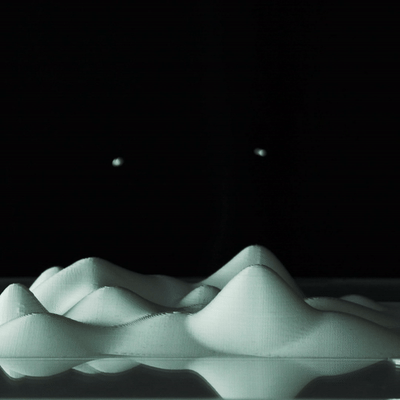 A dark scene with a small, illuminated model of a mountain range and two distant bright planets or stars in the sky.