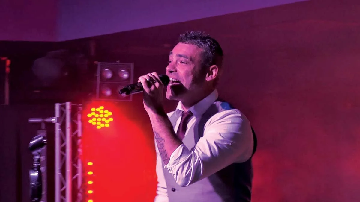 Male singer performing on stage with microphone, with red and purple lighting.