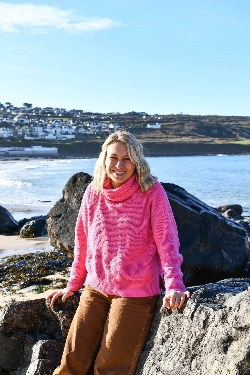 Jo Cave in a bright pink knit jumper on Porthmeor Beach, on a bright blue sky day