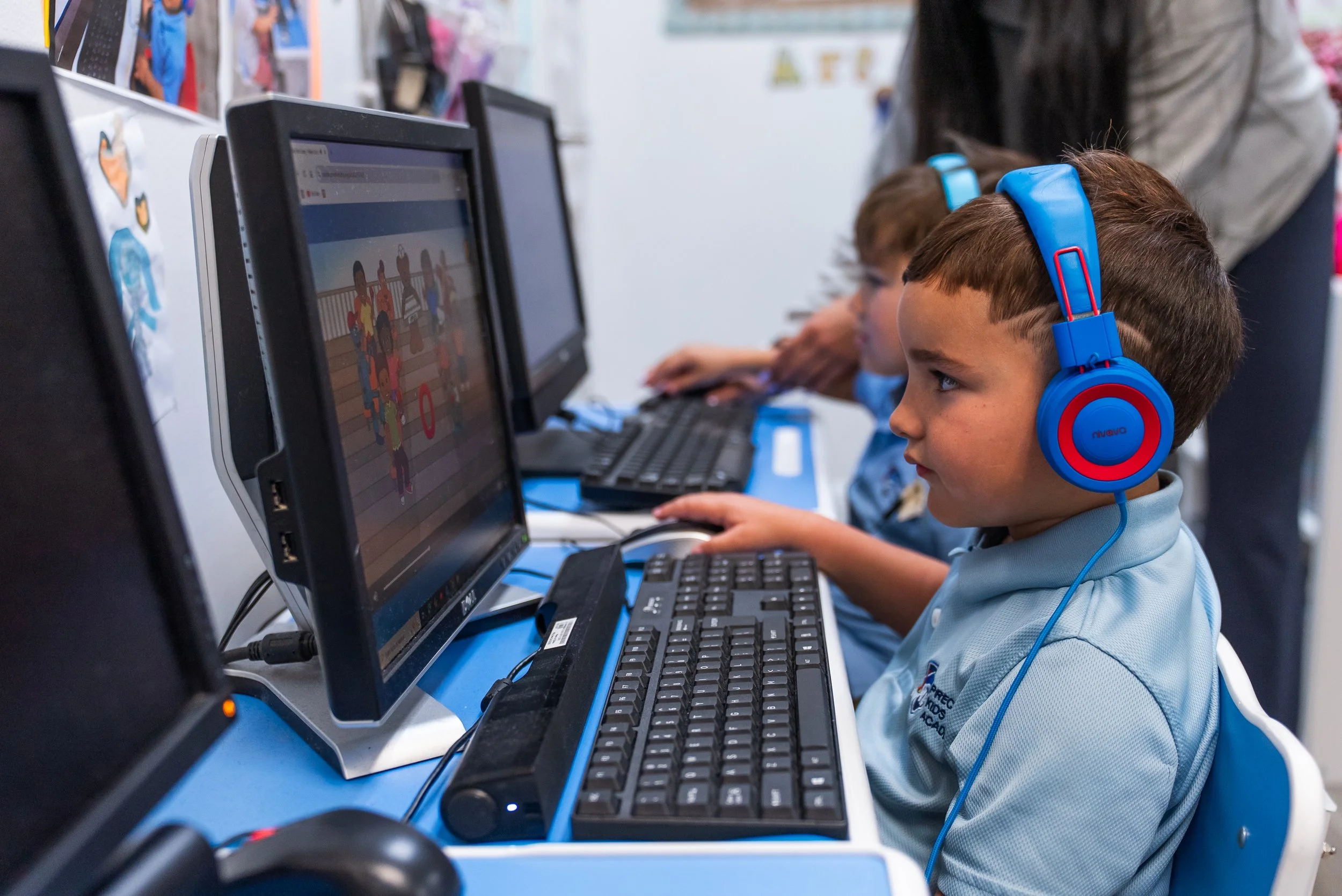 Children in a classroom engaged in using computers, with a focus on a young boy wearing blue headphones.