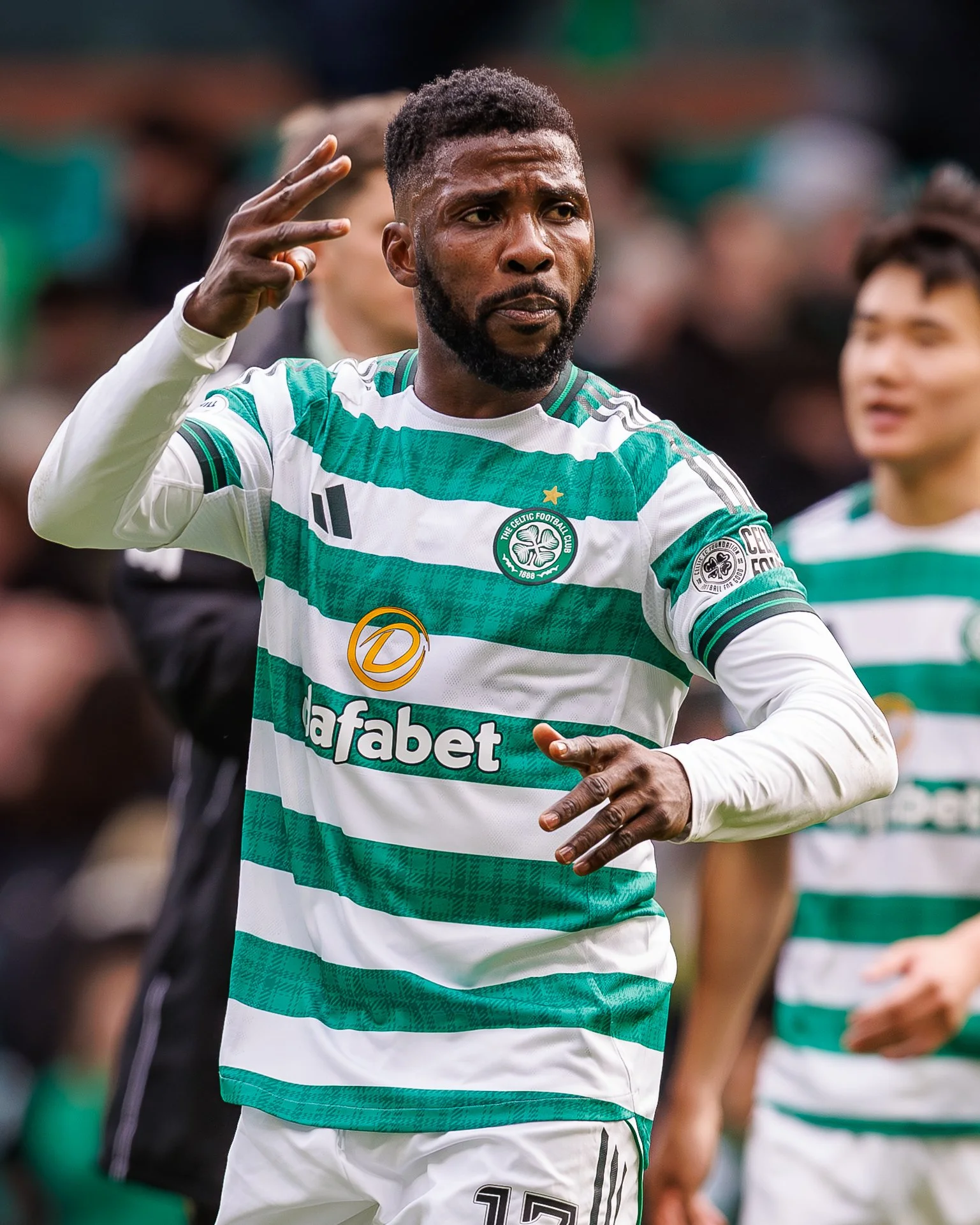 A soccer player wearing a green and white striped jersey with the number 17, making a peace sign with his right hand during a match.
