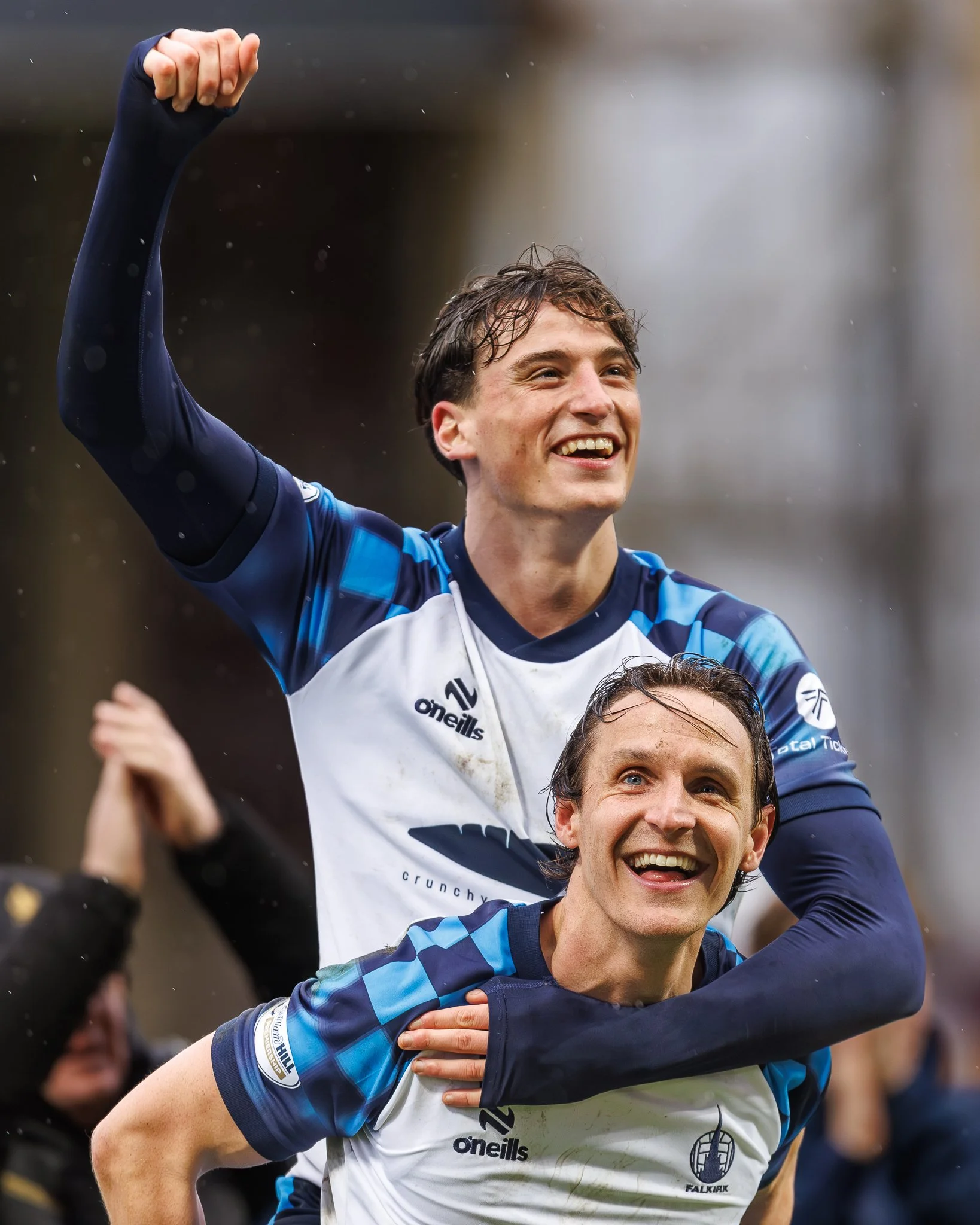 A rugby player in a white and blue jersey celebrating with a teammate during a match, with arms raised and smiling faces.
