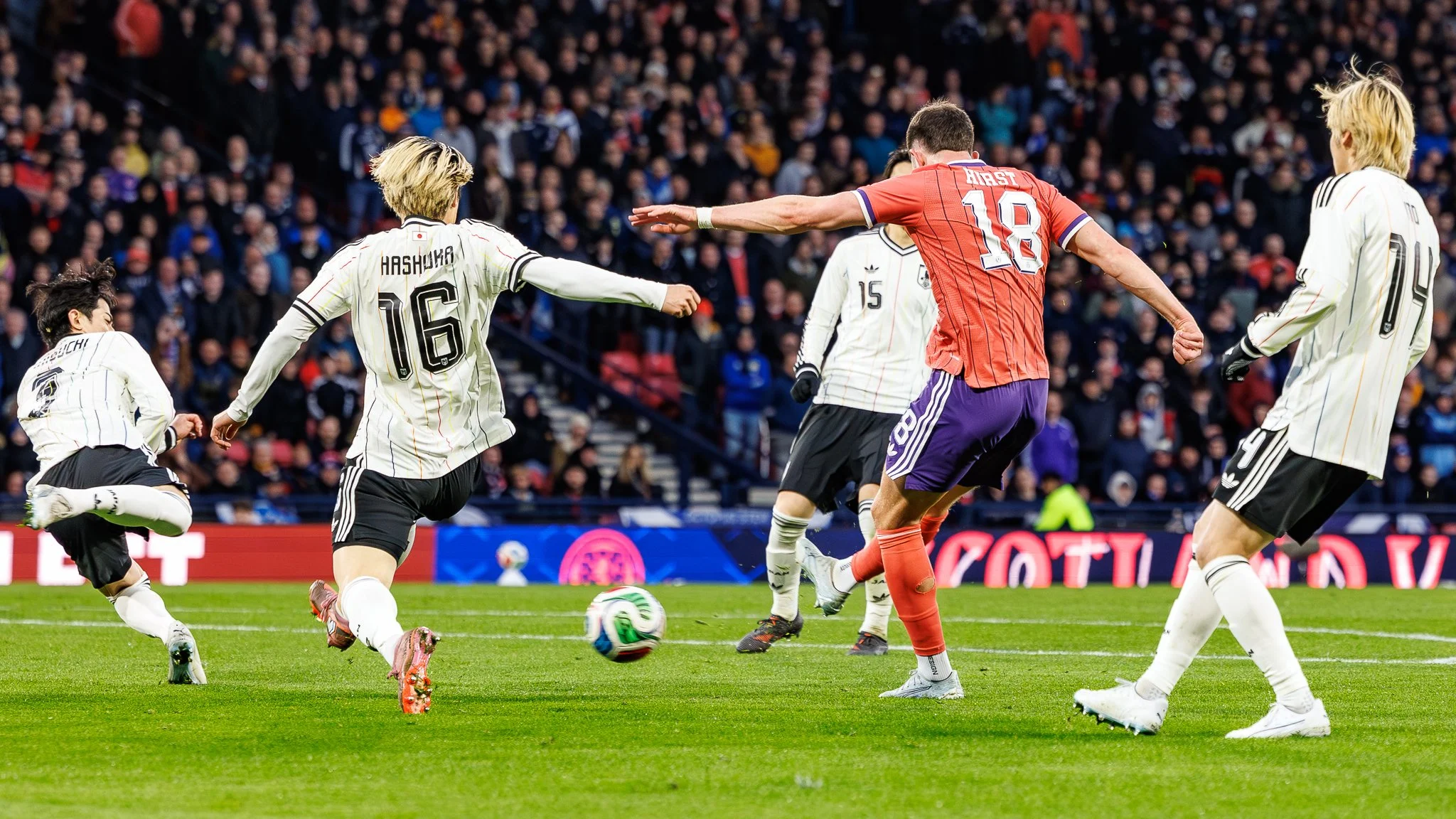 Soccer players competing for the ball during a match, with a crowd of spectators in the stands.