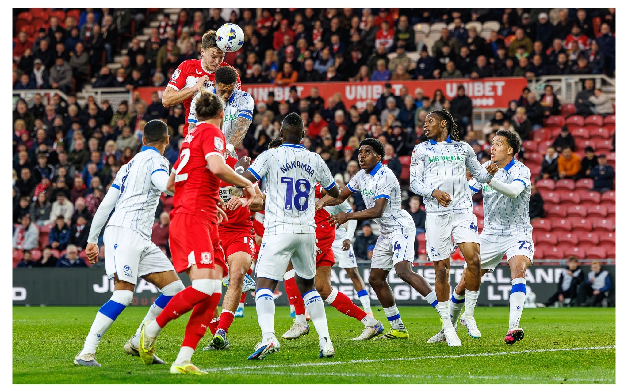 Soccer players in red and white uniforms competing for the ball during a match with a crowd watching in the background
