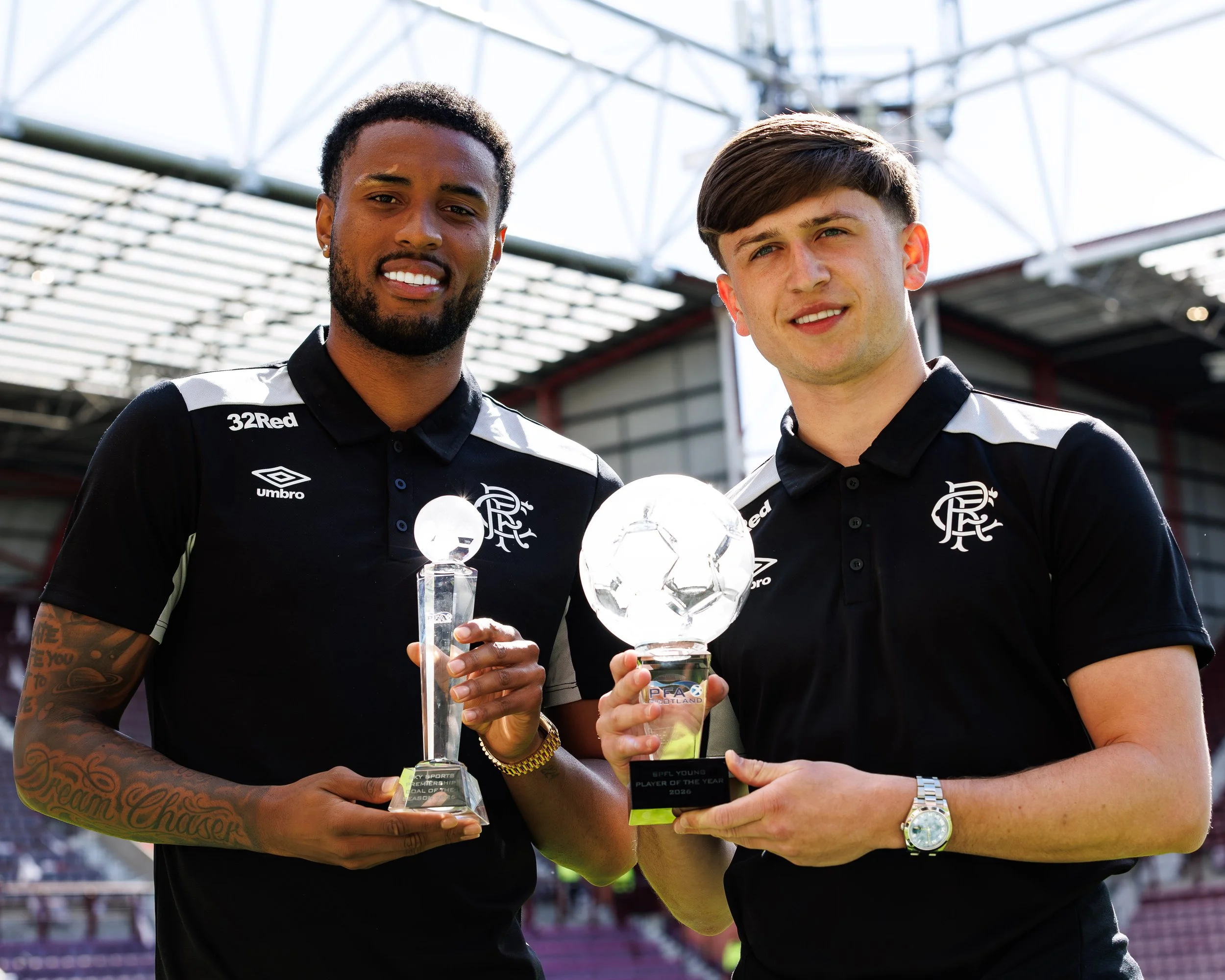 Two young soccer players in black and white uniforms holding trophies and awards at a stadium celebration.
