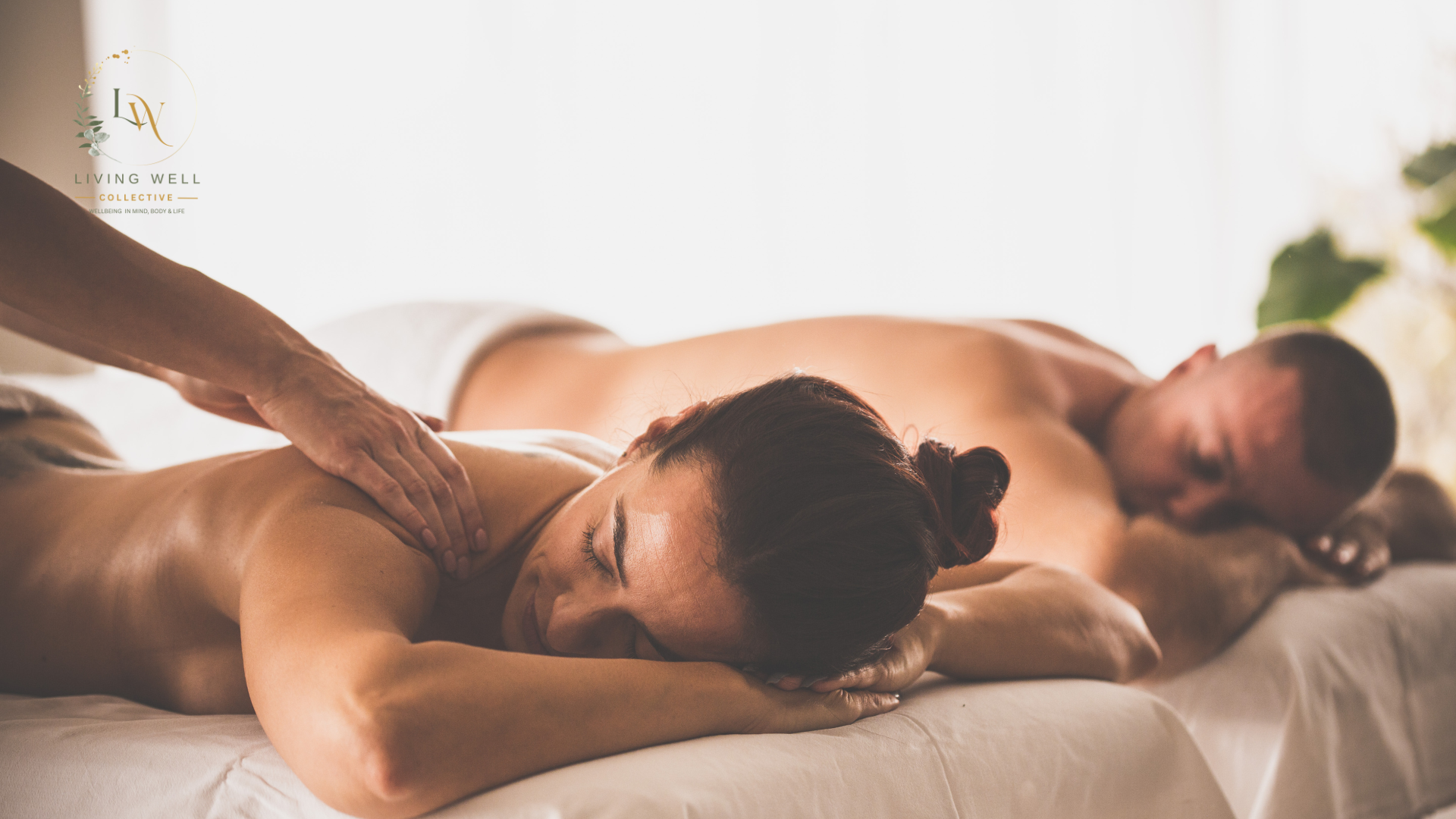 Two people lying face down on massage tables, receiving a massage from therapists in a serene, softly lit room.