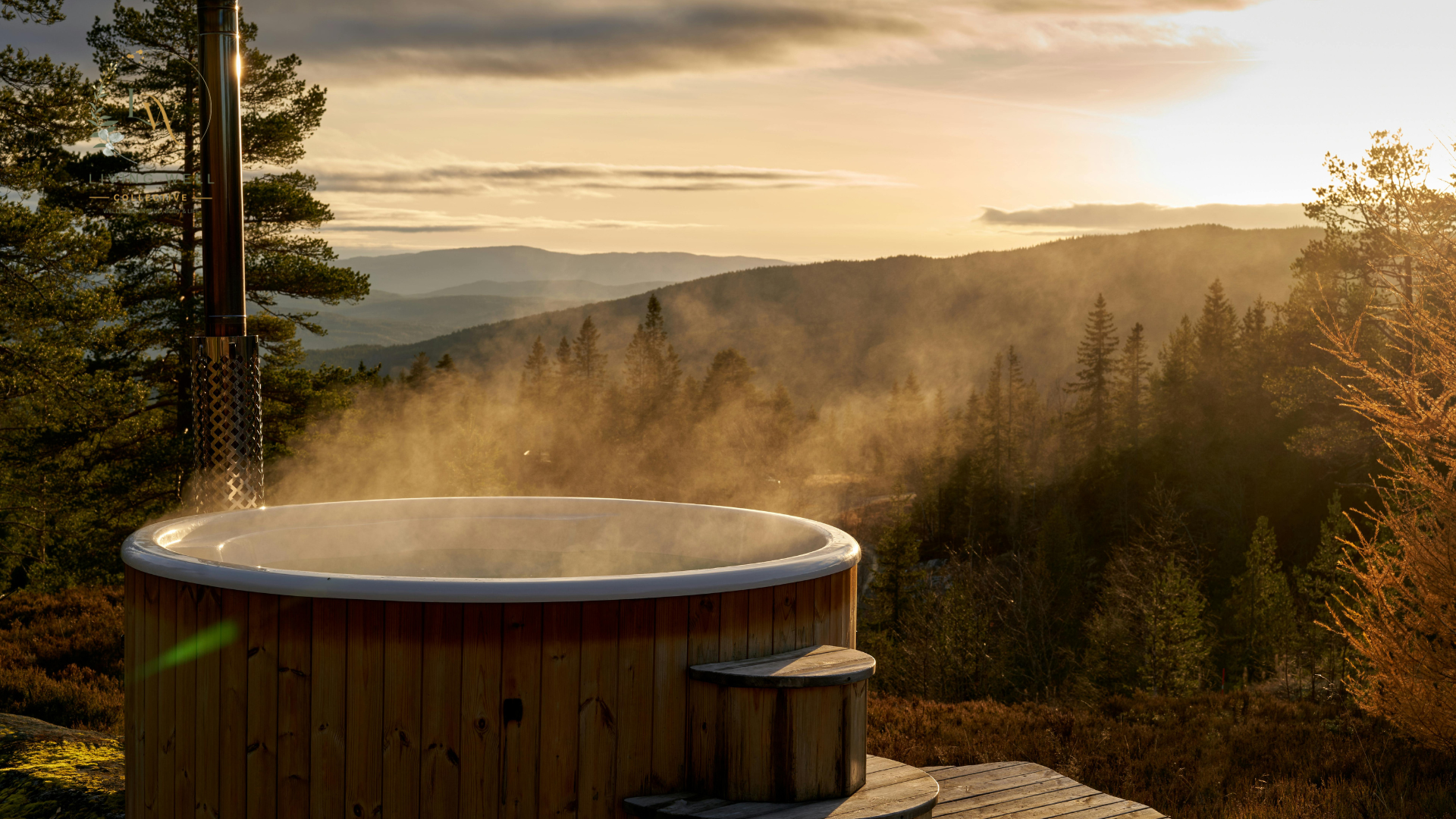 Wooden hot tub on deck overlooking a forested mountain landscape during sunset with steam rising from the hot tub.