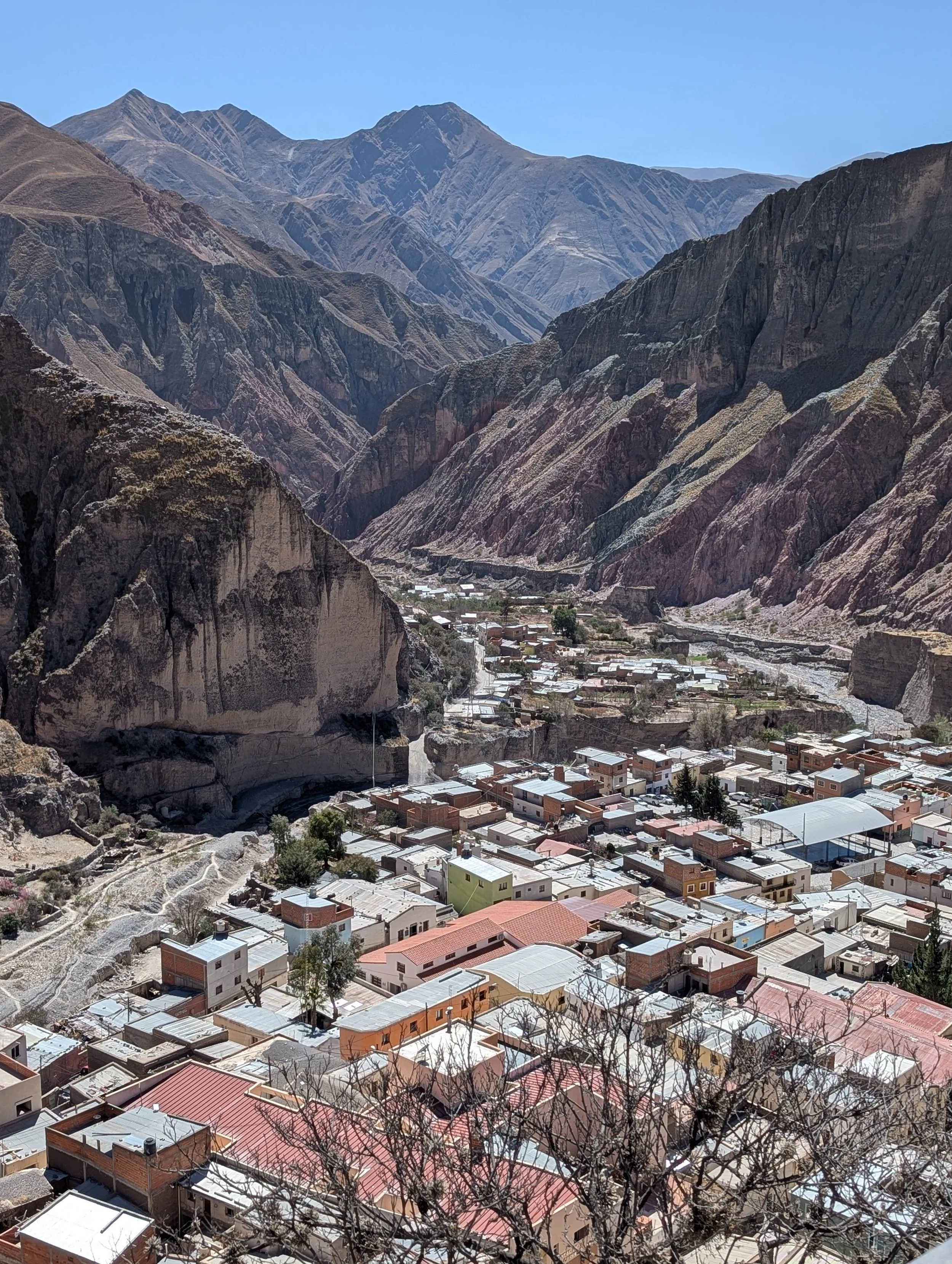 Iruja, Argentina. A view of a small town situated in a valley surrounded by rugged, steep mountains with dry, rocky terrain under a clear blue sky.