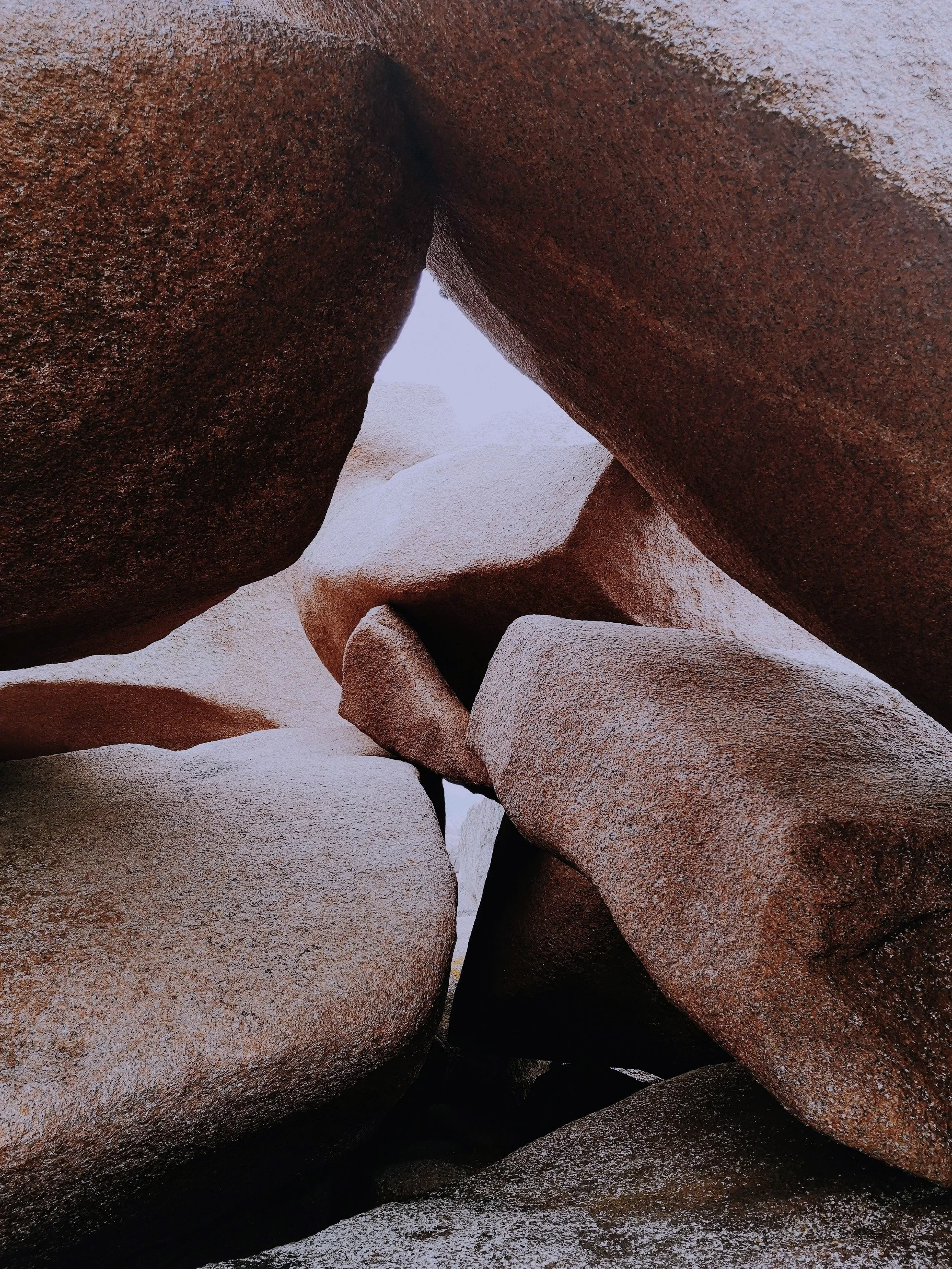 Close-up view of large, angular red-brown rocks with rough textures, forming a narrow passage or crevice.