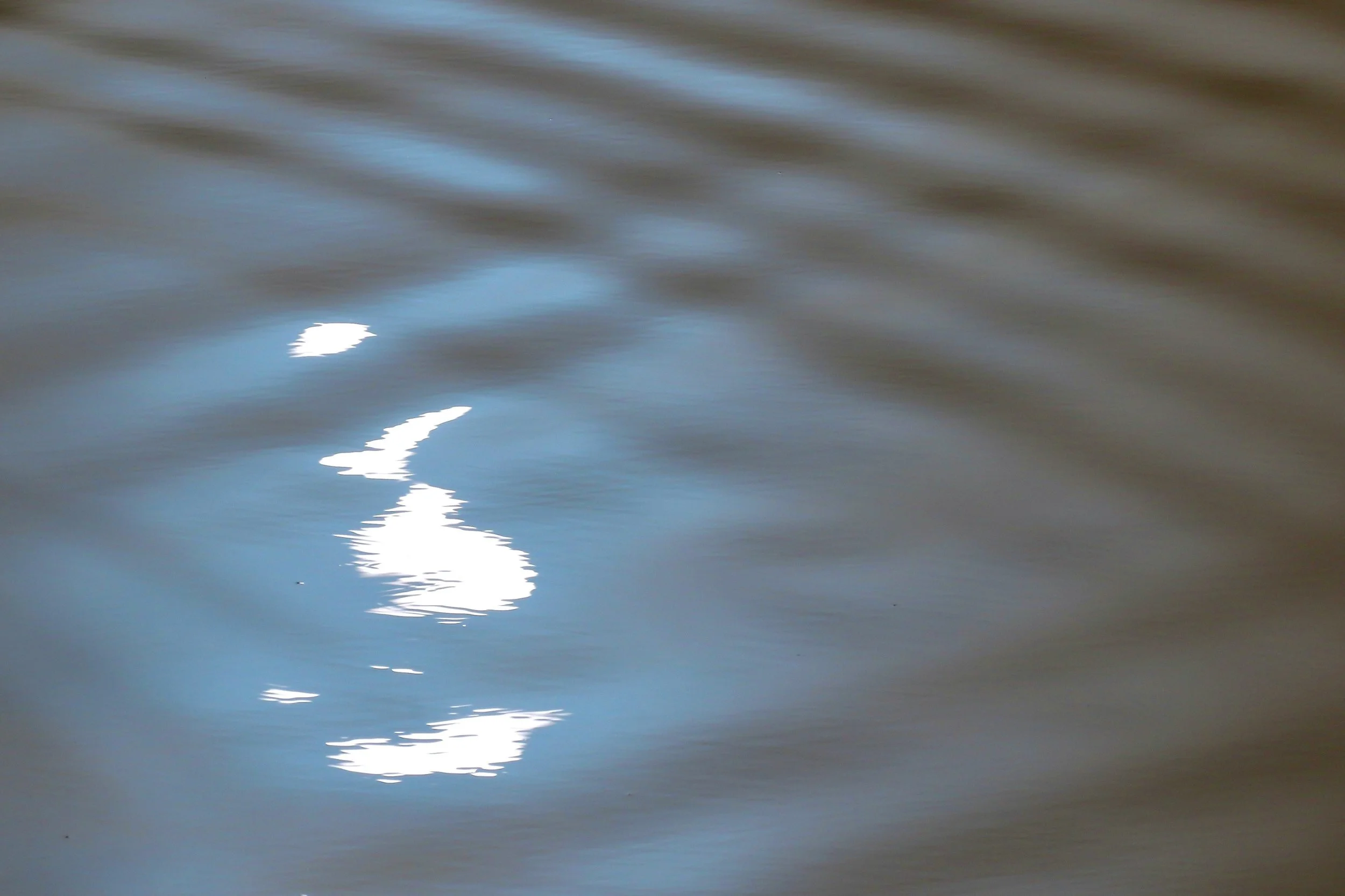 Reflected sunlight on water with ripples and shadows.