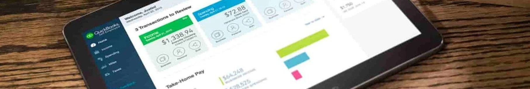 A smartphone displaying a financial app with green, blue, and pink color sections, showing transactions, income, expenses, and a bar graph, placed on a wooden surface.
