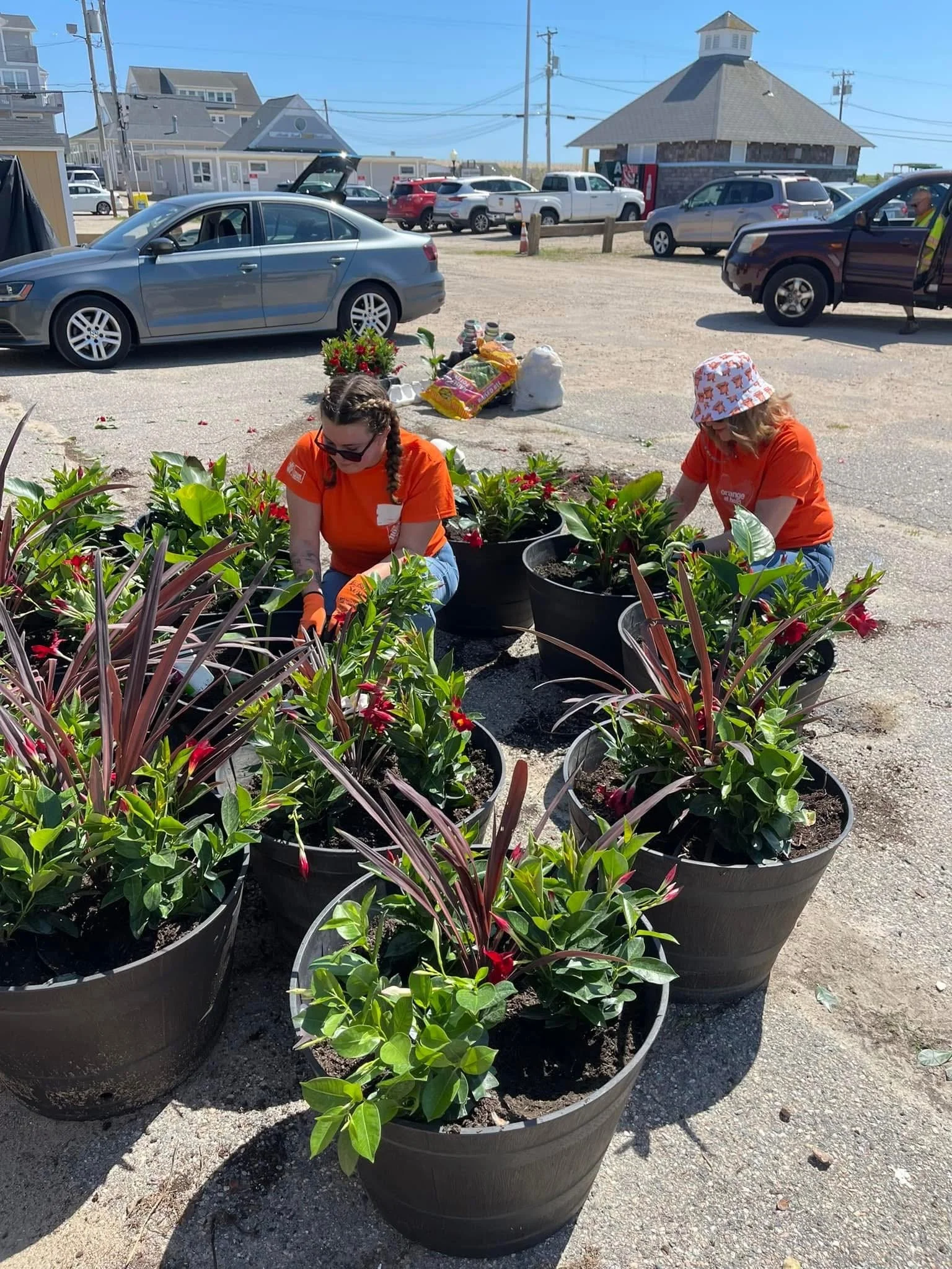 Two women are planting flowers in large black pots outdoors from Home Depot in Westerly, RI