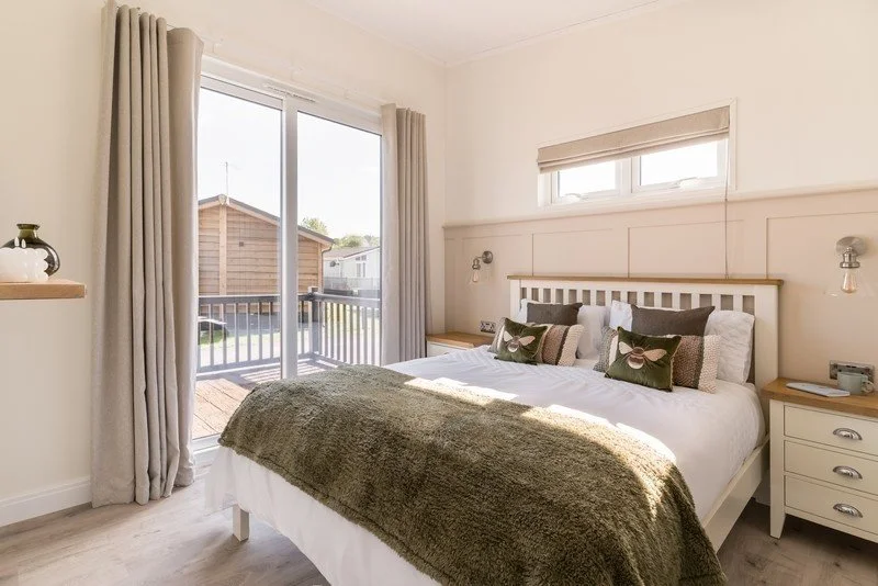 Bright bedroom with a large bed, beige curtains, sliding glass door leading to a deck, and a sleeping porch window, decorated with neutral tones and minimalist decor.