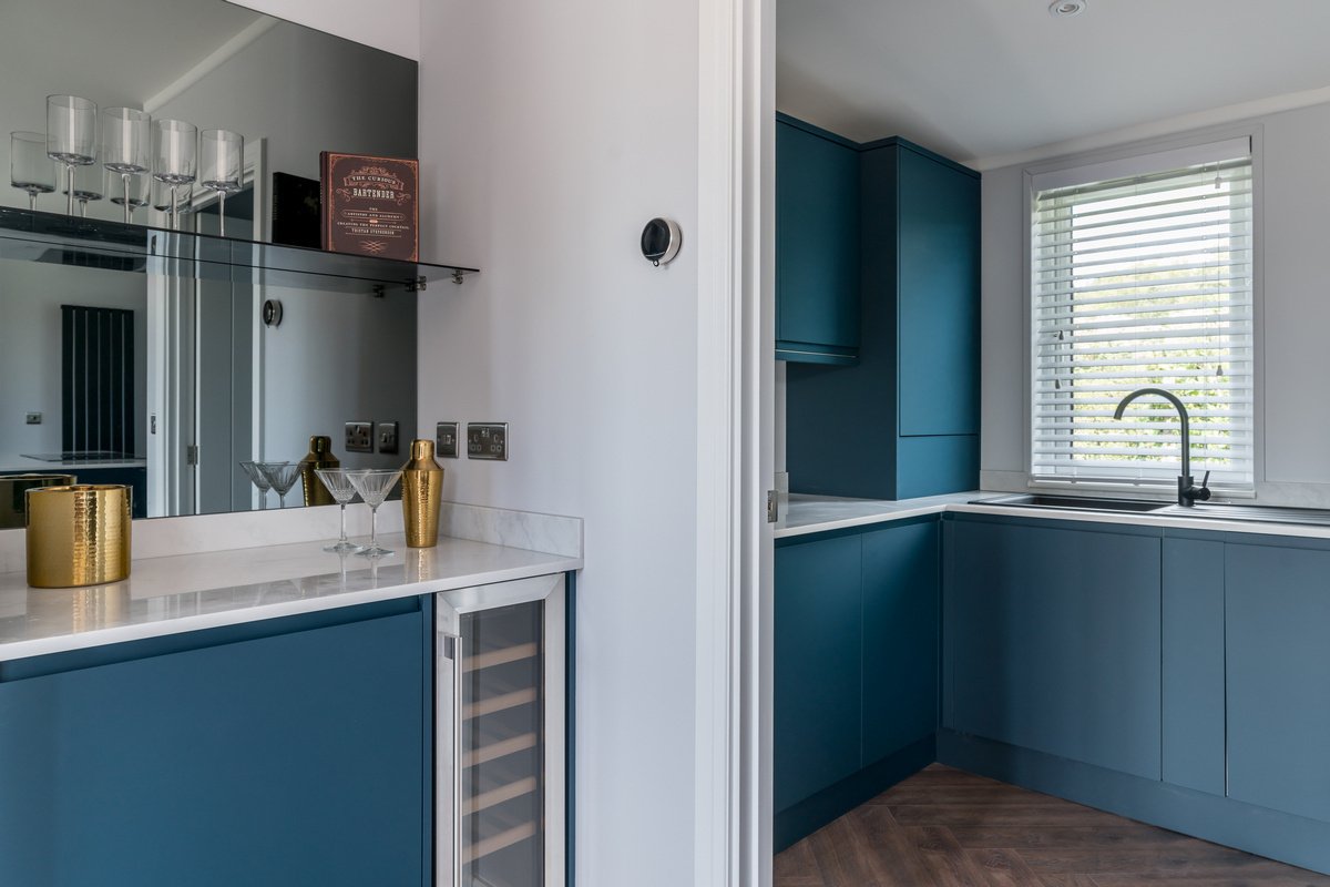 A modern kitchen with blue cabinets, a white marble countertop, and a window with white blinds.