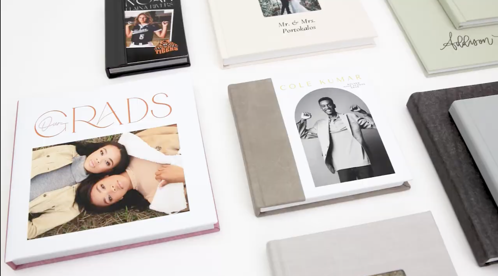 Books and photo albums spread out on a white surface, including a photo book titled 'Our GradS' with a cover photo of two young women lying on the ground.