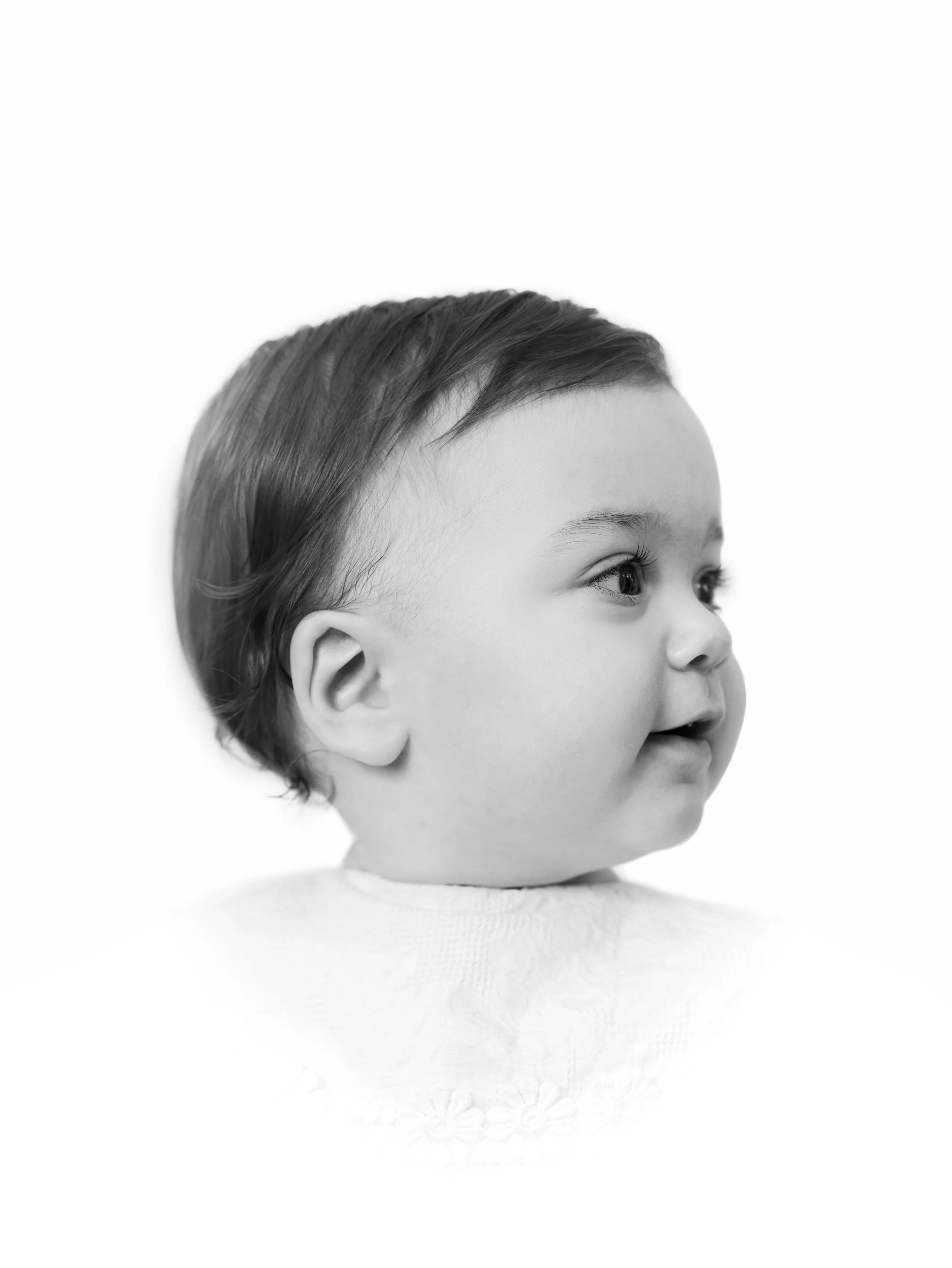A black and white close-up photograph of a toddler's head, with short, neatly combed hair, looking slightly upward and to the right against a plain white background.