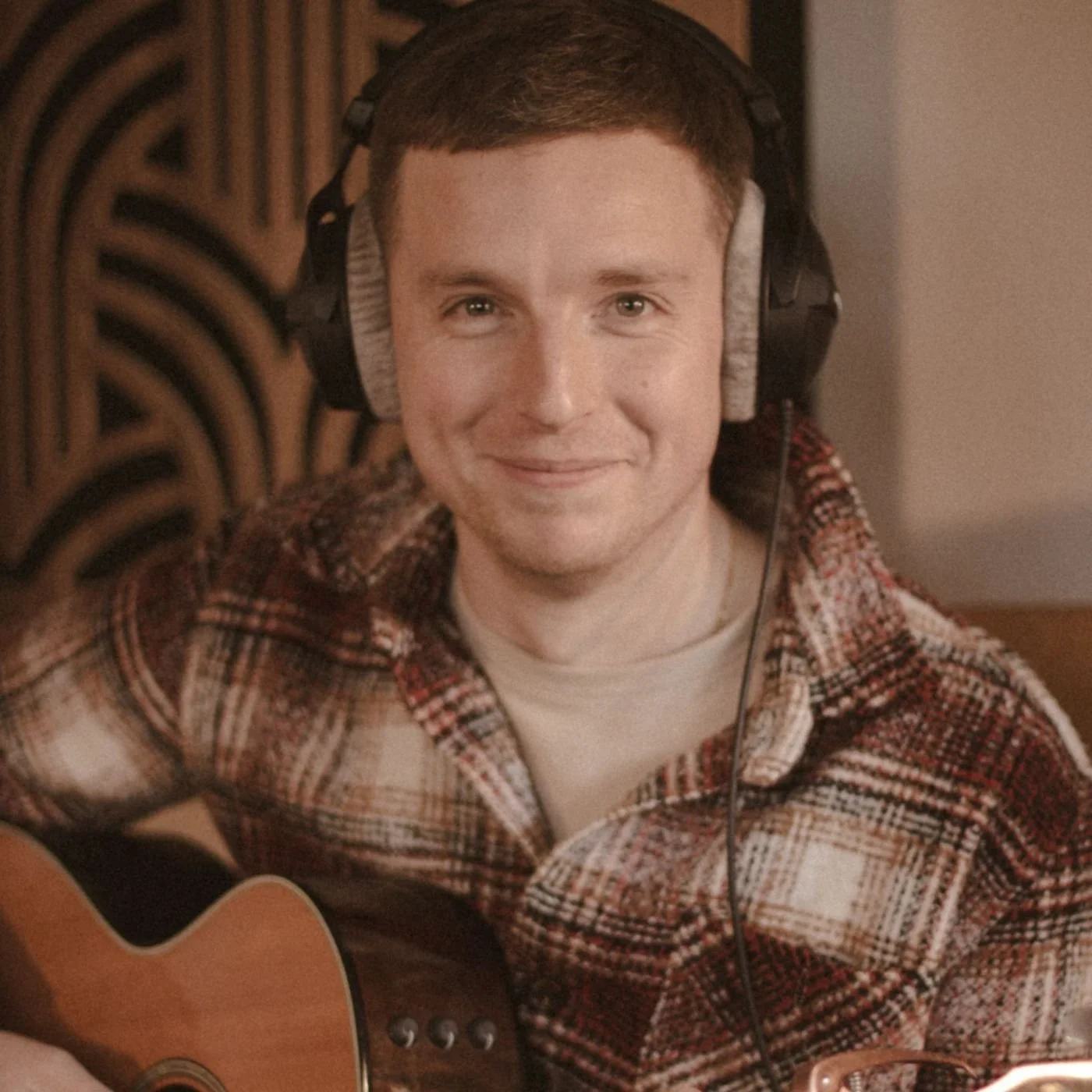 UK songwriter Adam Kirkup in the studio with an acoustic guitar and headphones, ready to record your custom song.