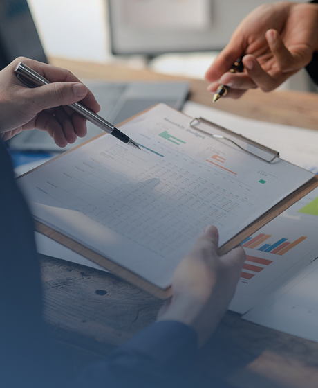 Two people discussing financial data on a clipboard and documents with charts on a wooden table.