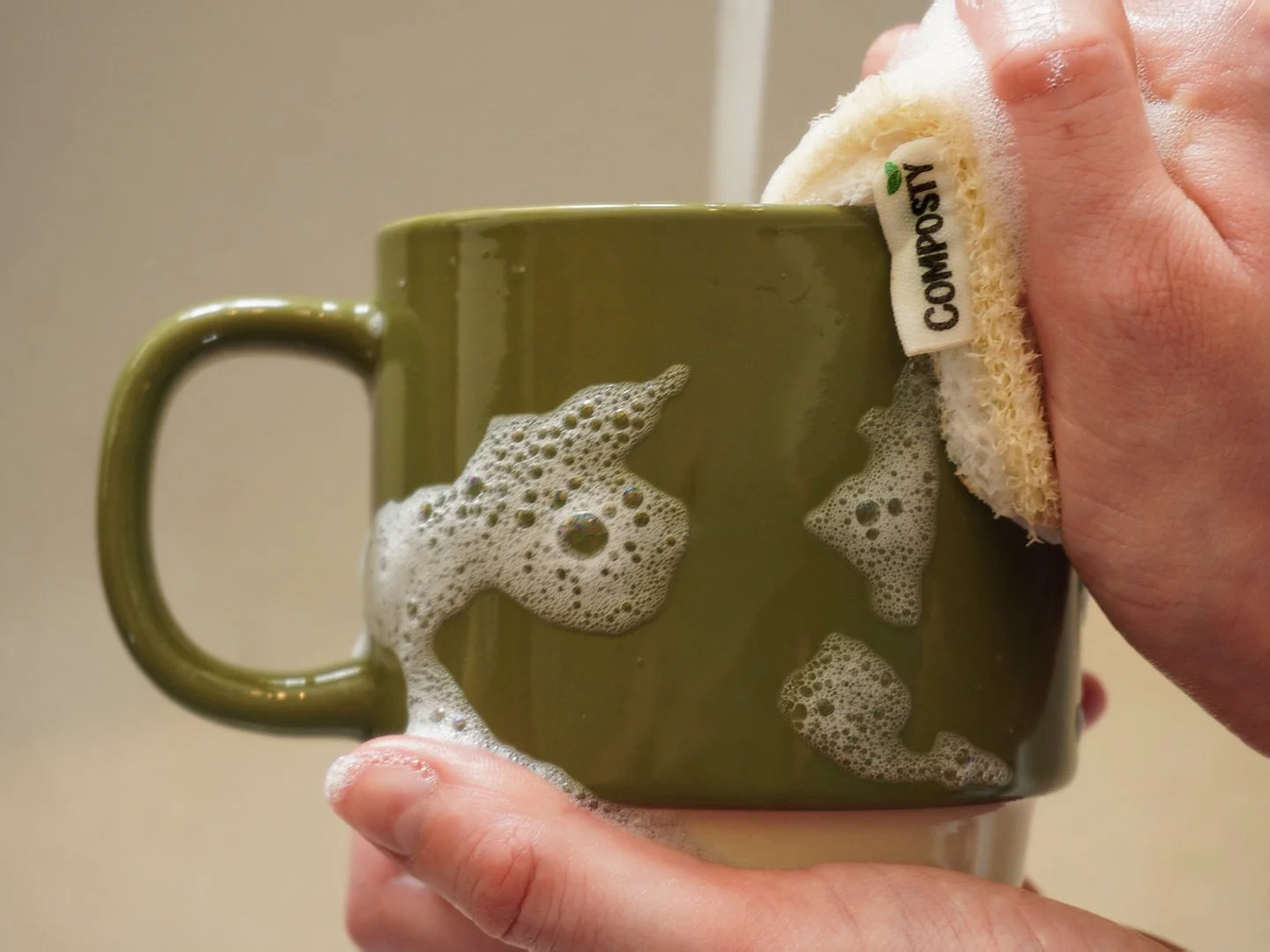 Hands washing an olive green ceramic mug with a soapy Composty eco-friendly sponge, shot by Emma Burton Studio