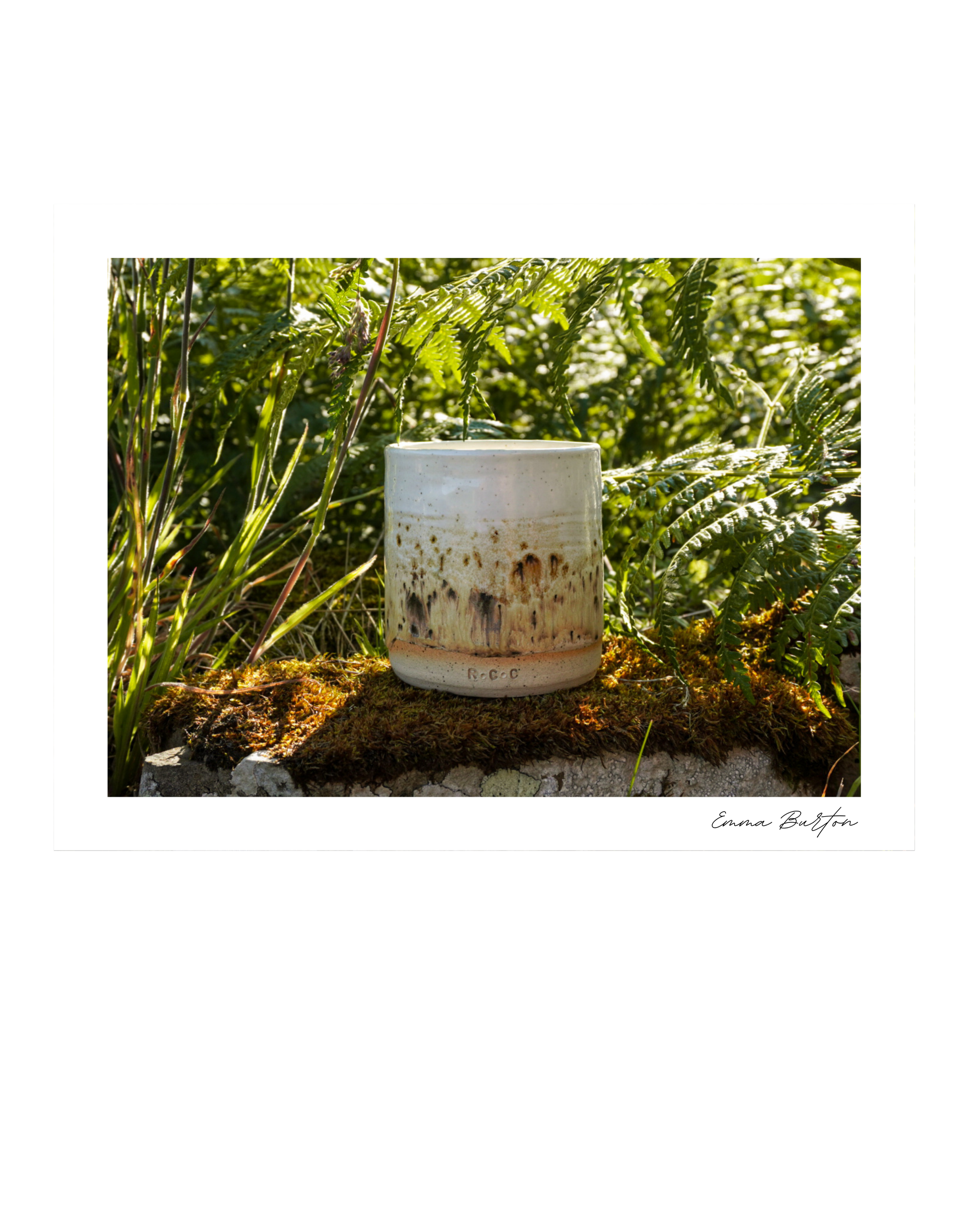 A white Restorative Candle Company ceramic cup sitting on mossy ground in a lush green outdoor setting with tall ferns, shot by Emma Burton Studio in the Scottish Highlands.