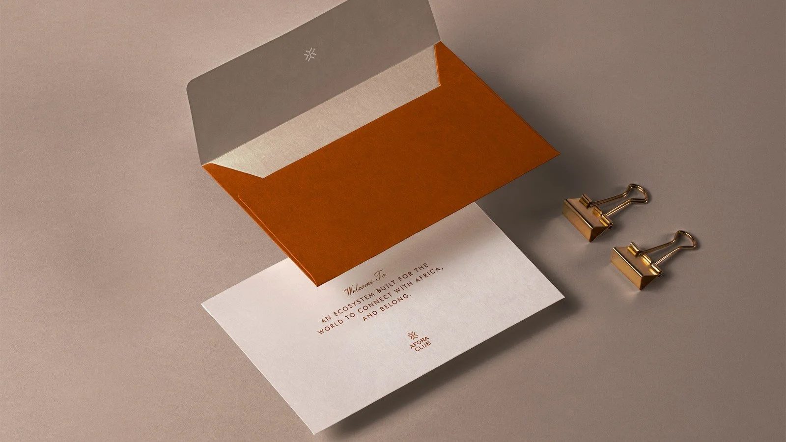 White paper with red and black text, resting on a neutral surface, partially covered by an orange and grey folder or envelope, with two gold binder clips nearby.