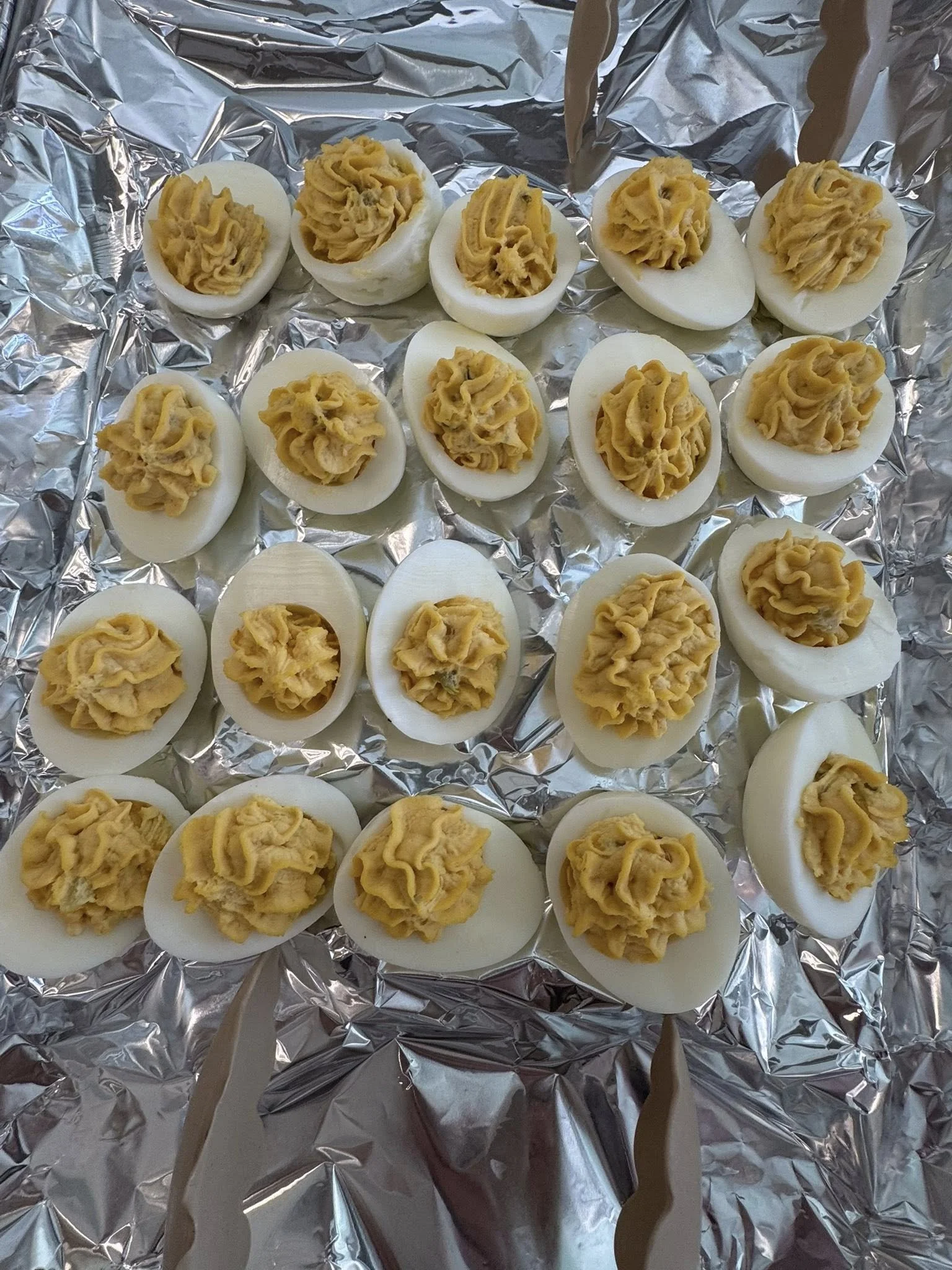 A collection of halved hard-boiled eggs with a piped yellow filling on top, arranged on crinkled aluminum foil.
