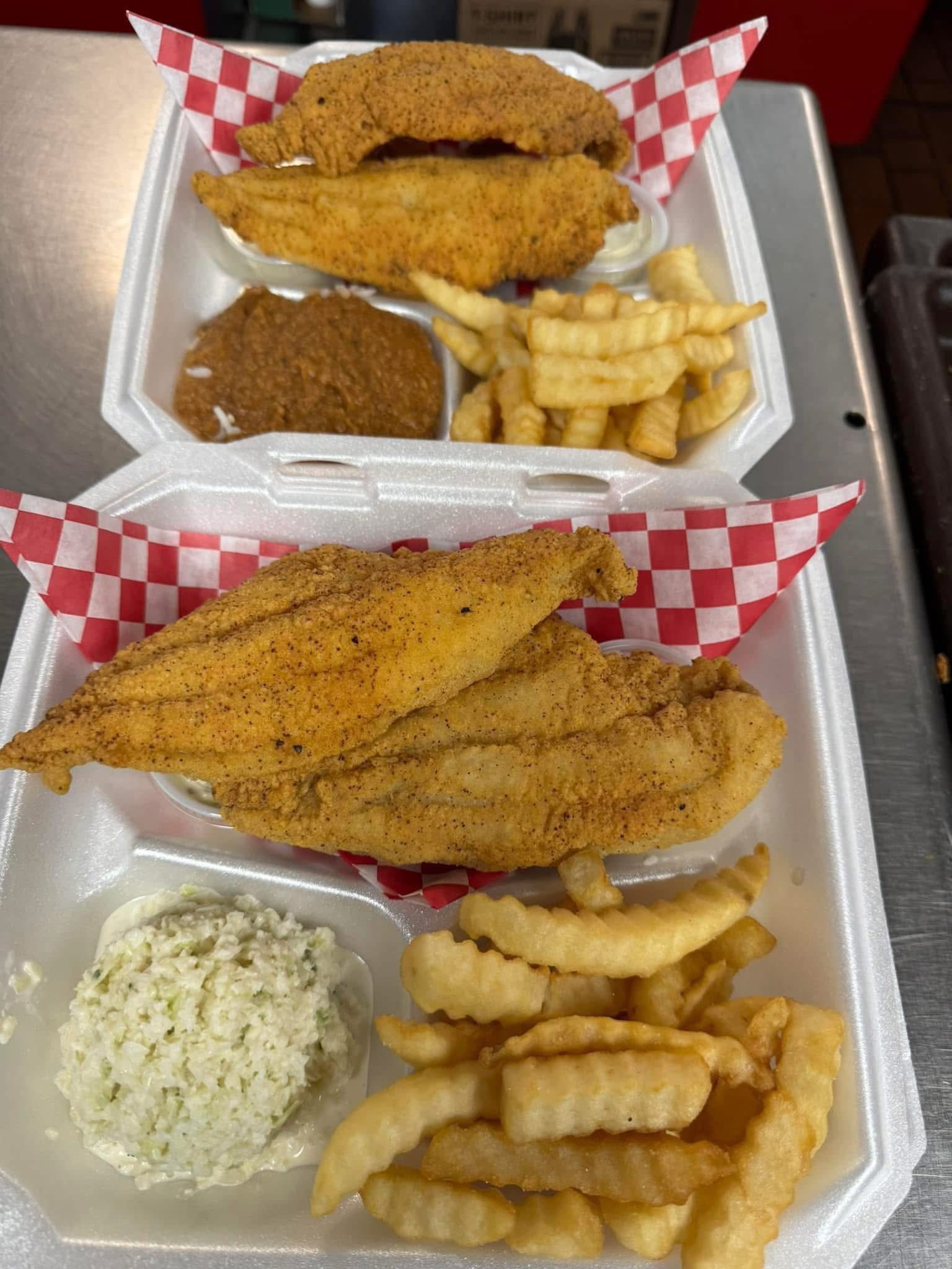 A styrofoam tray with fried fish fillets, crinkle-cut French fries, coleslaw, and a serving of brown gravy.
