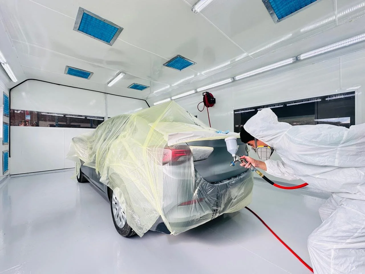 Persona que usa equipo de protección trabajando en el pintado de un automóvil en una cabina de pintura.