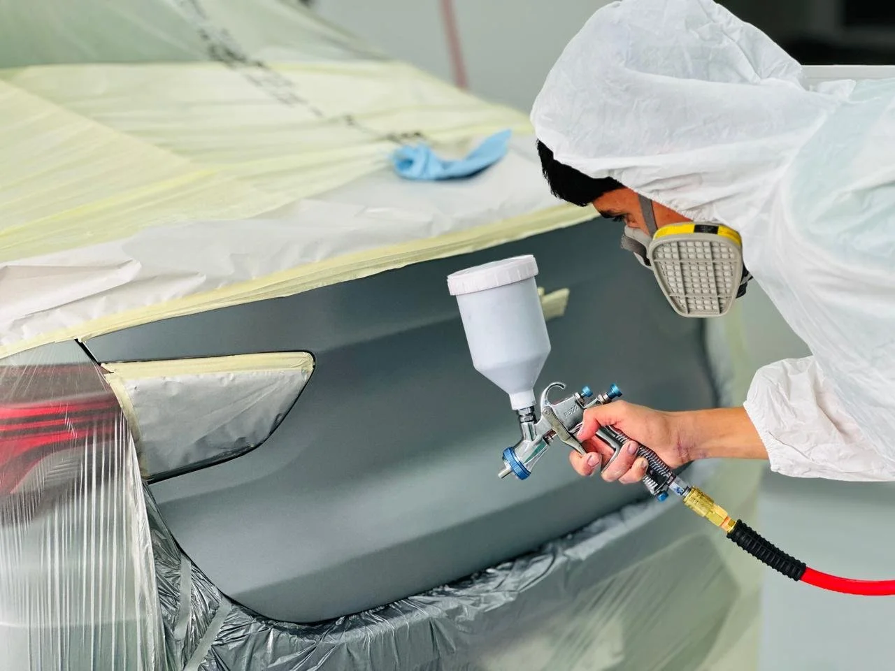 Persona vistiendo protección y rociando pintura en una superficie de automóvil.