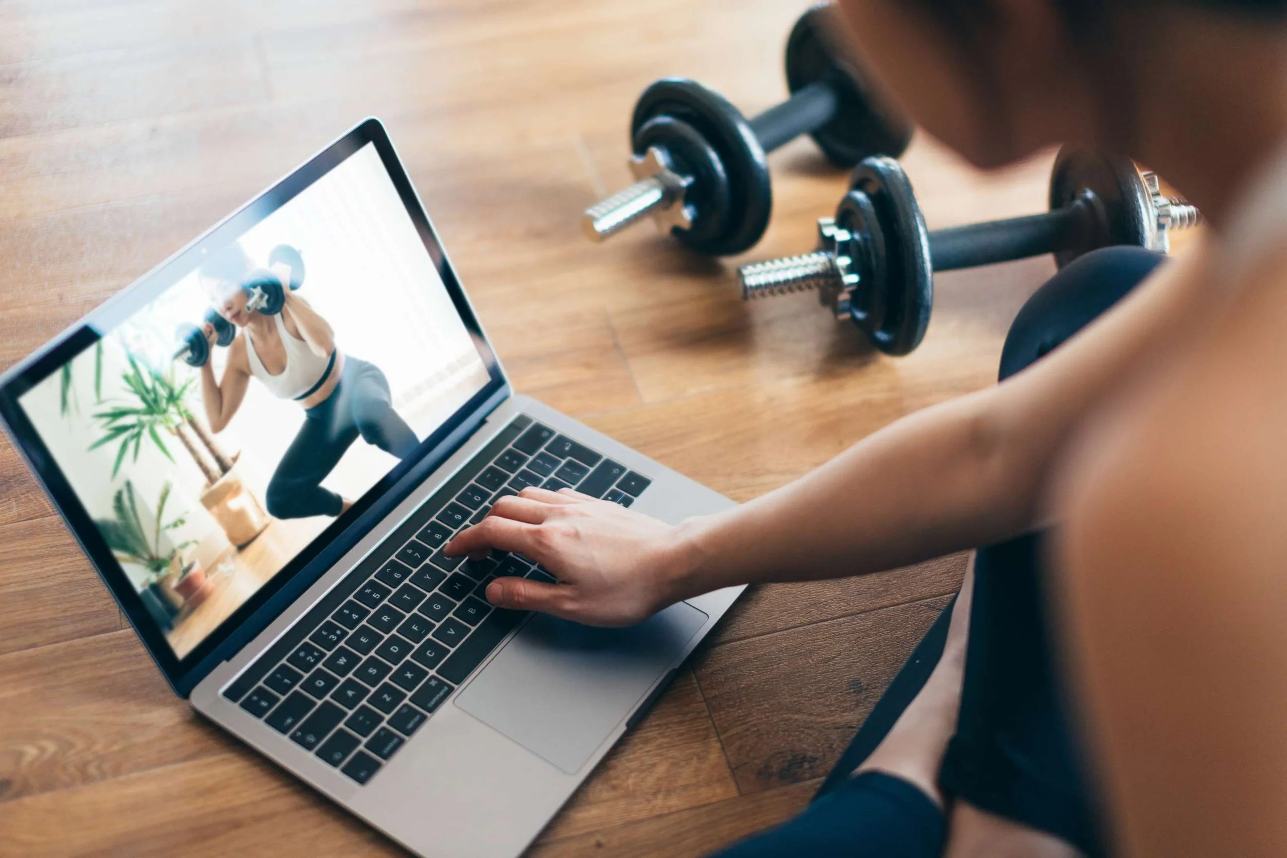 Client participating in a virtual personal training session from home using a laptop and dumbbells.