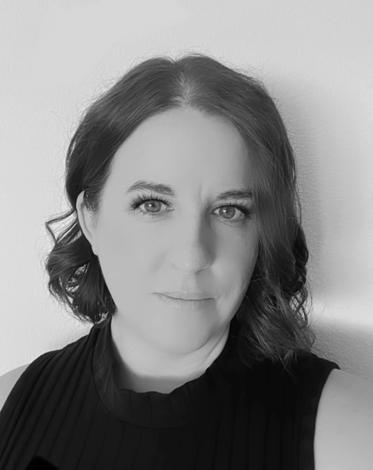 Black and white portrait of a woman with dark, wavy hair and piercing eyes, wearing a sleeveless top.