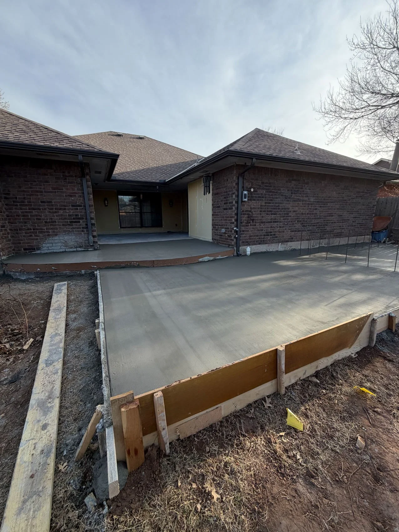 Backyard of a house under construction with freshly poured concrete for a walkway, surrounded by wooden formwork.