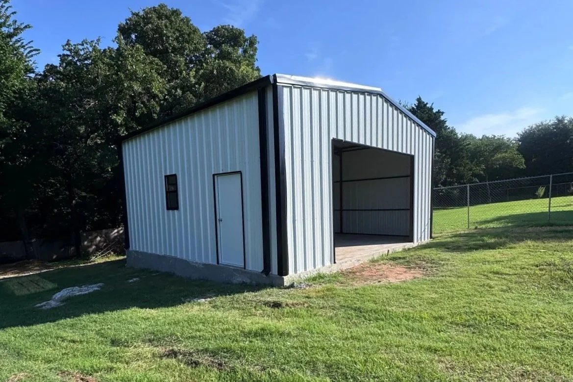 A gray metal storage shed with a courtyard and a backdrop of trees under a blue sky.