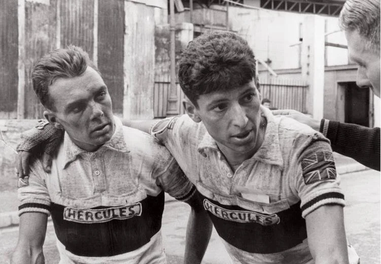 Two young men with team name 'Hercules' on their shirts, being consoled by an older man, in an industrial setting, black and white photo.