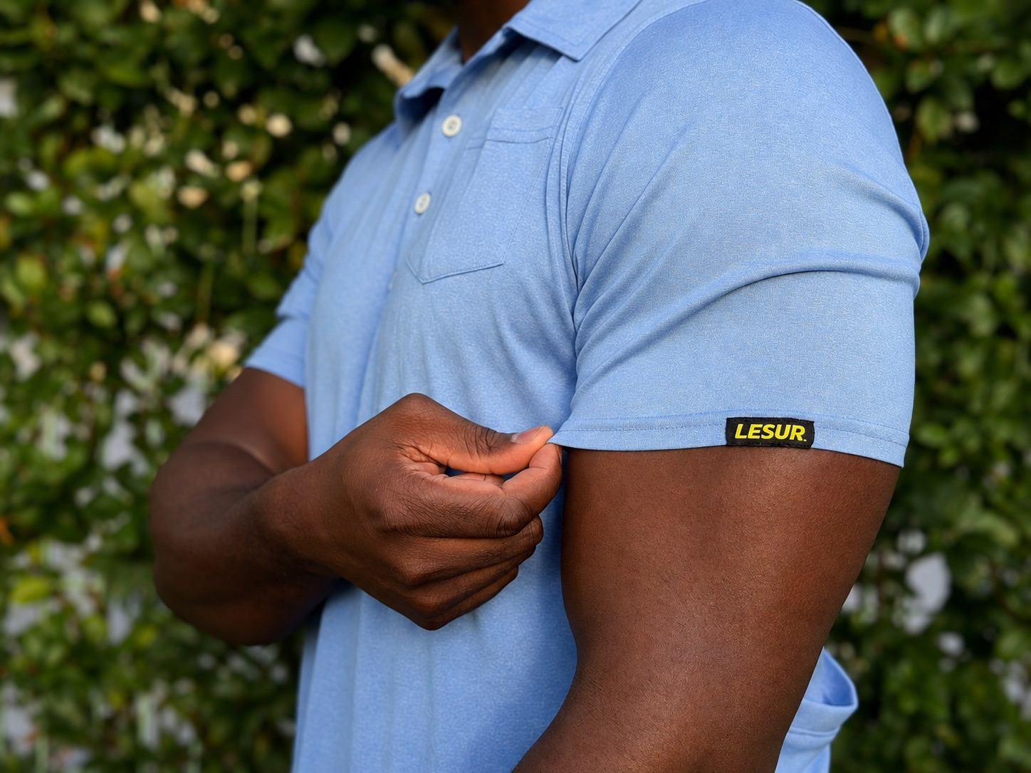Close-up of a man wearing a light blue polo shirt with a LESUR sleeve label