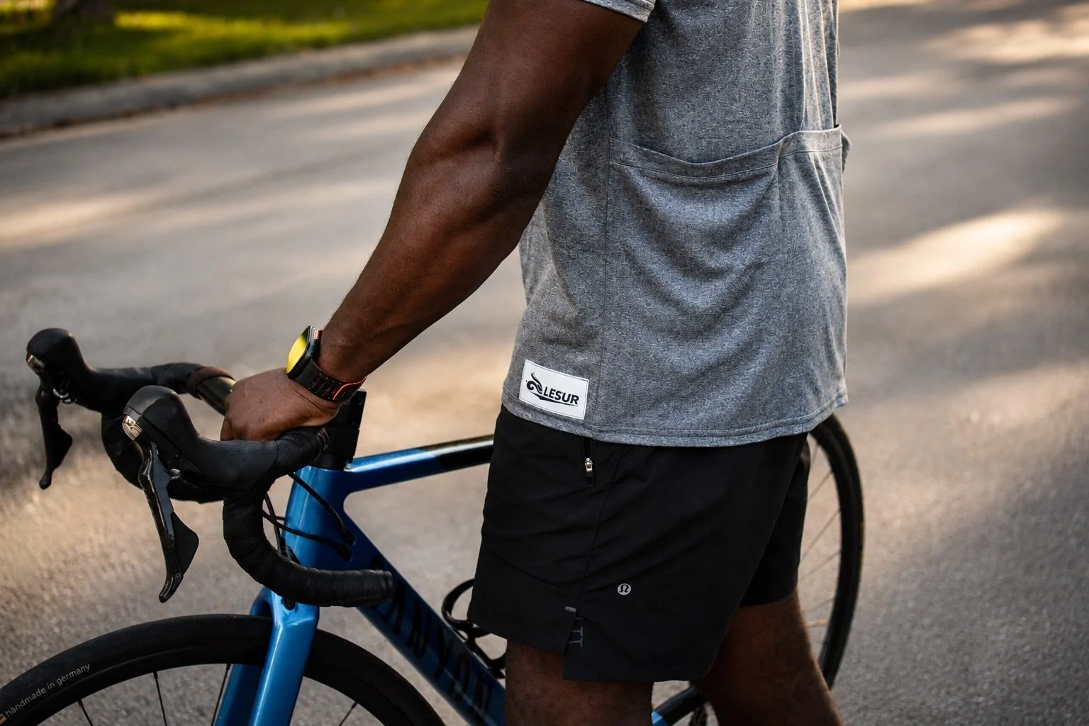 Cyclist wearing a gray shirt and black shorts holding the handlebars of a blue road bike outdoors