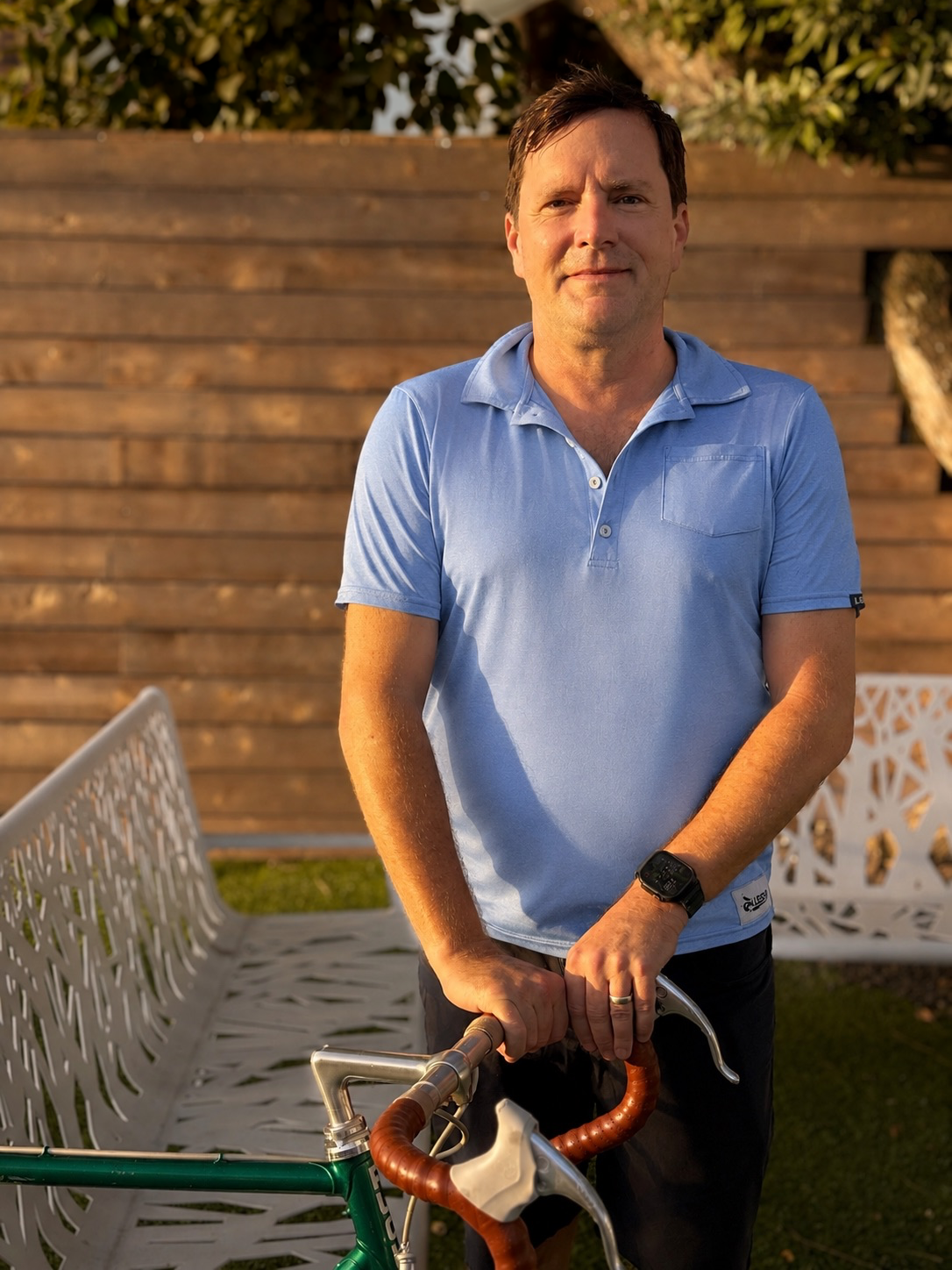 Man in a light blue polo shirt standing outdoors with a vintage green bicycle.