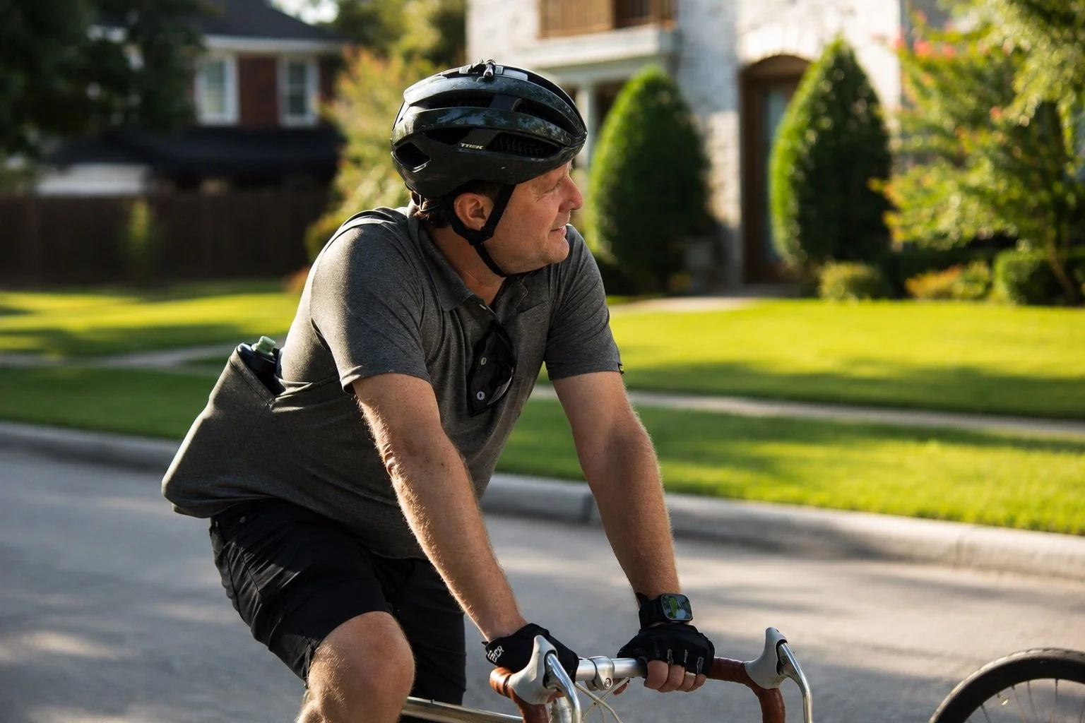 Cyclist wearing a helmet and gloves rides a road bike through a sunny residential neighborhood.