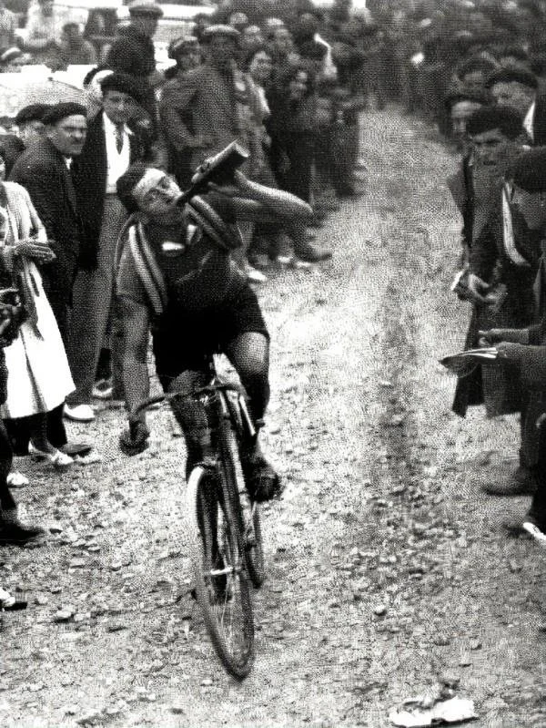 Vintage black-and-white photo of a cyclist riding through a crowded street as spectators watch.